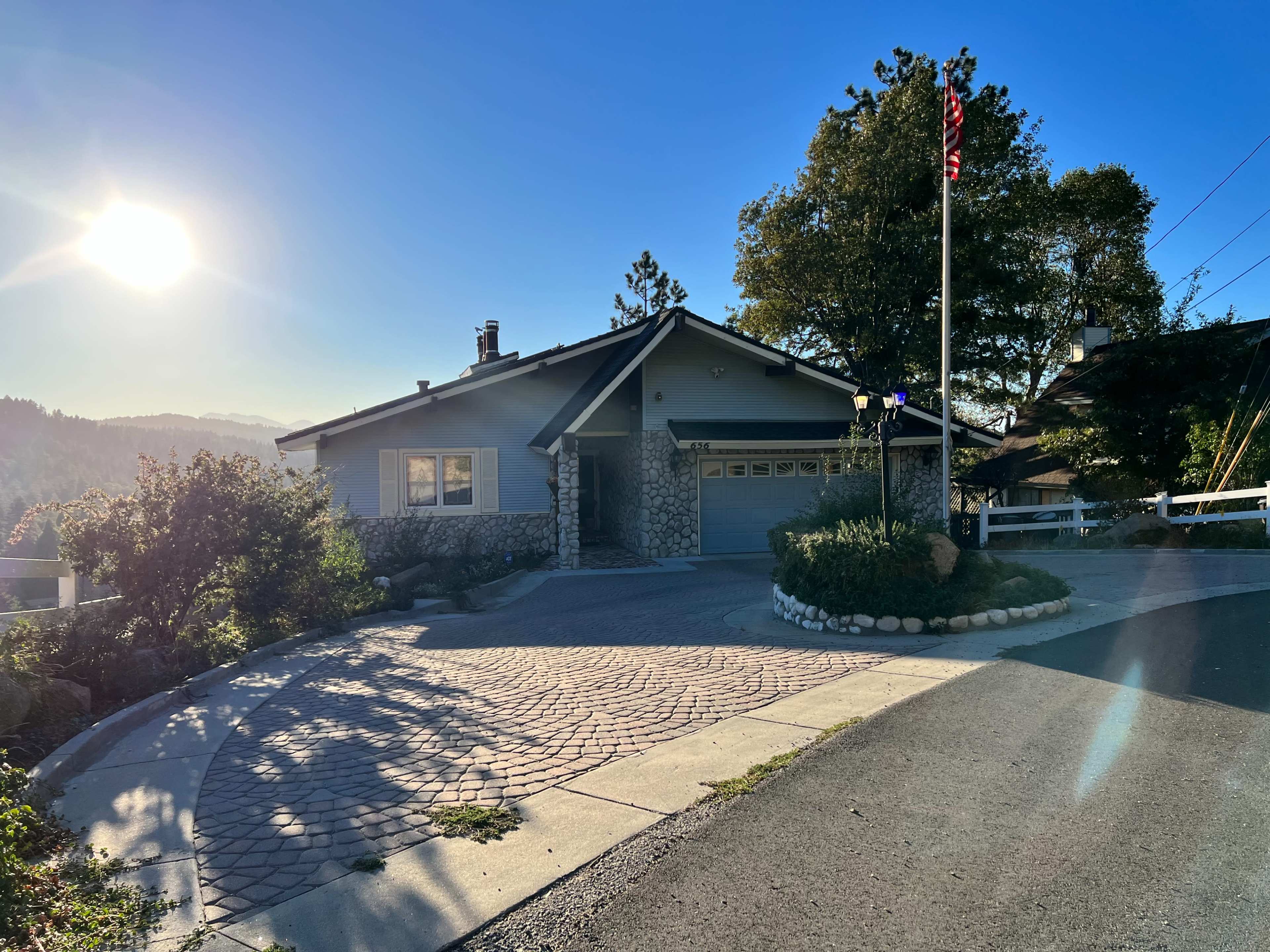 A modern house with a stone facade and a front driveway illuminated by the late afternoon sun is situated on a corner lot.