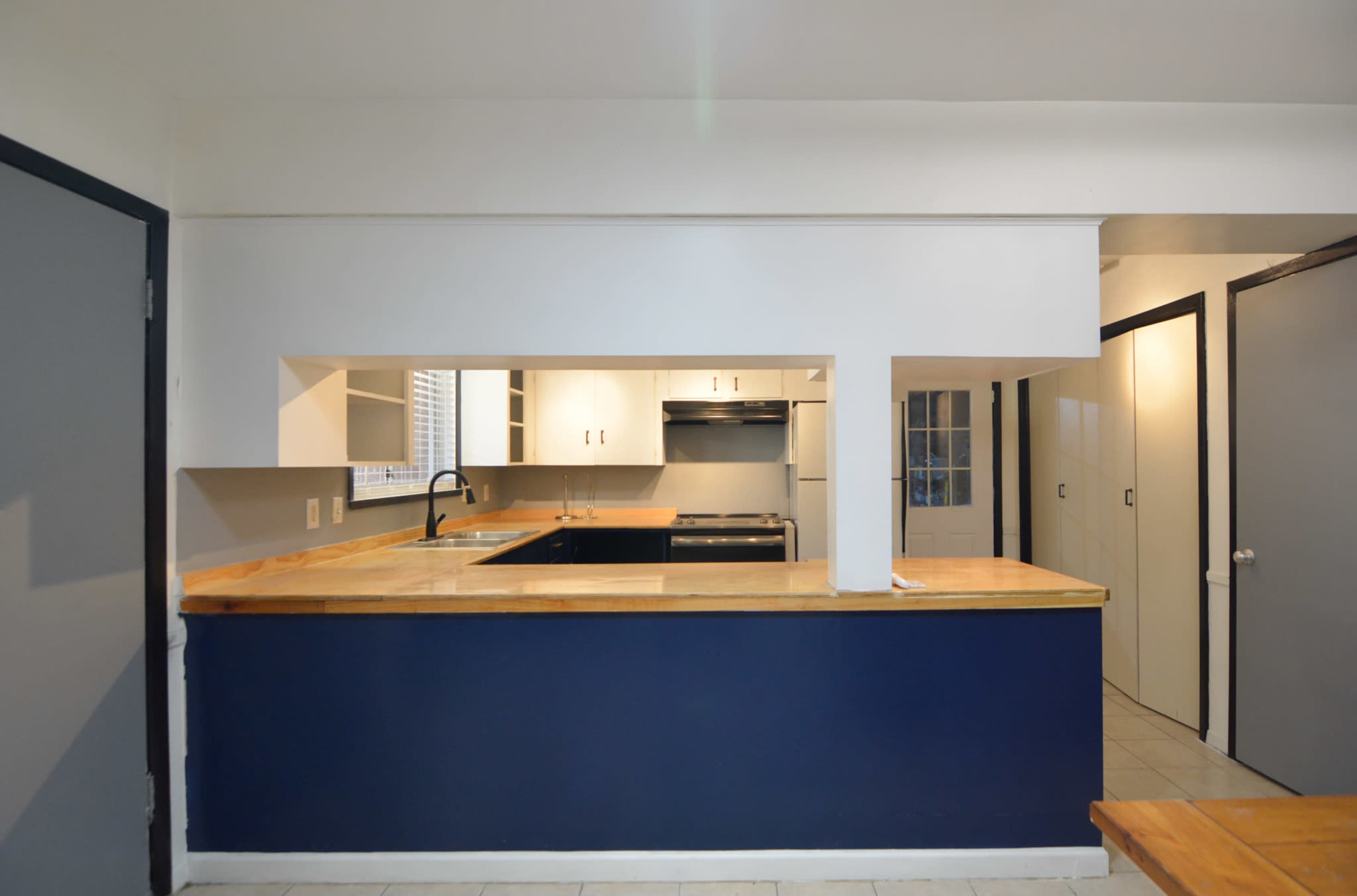 A kitchen with a central island featuring a wooden countertop, white cabinets, and a doorway leading to another room.