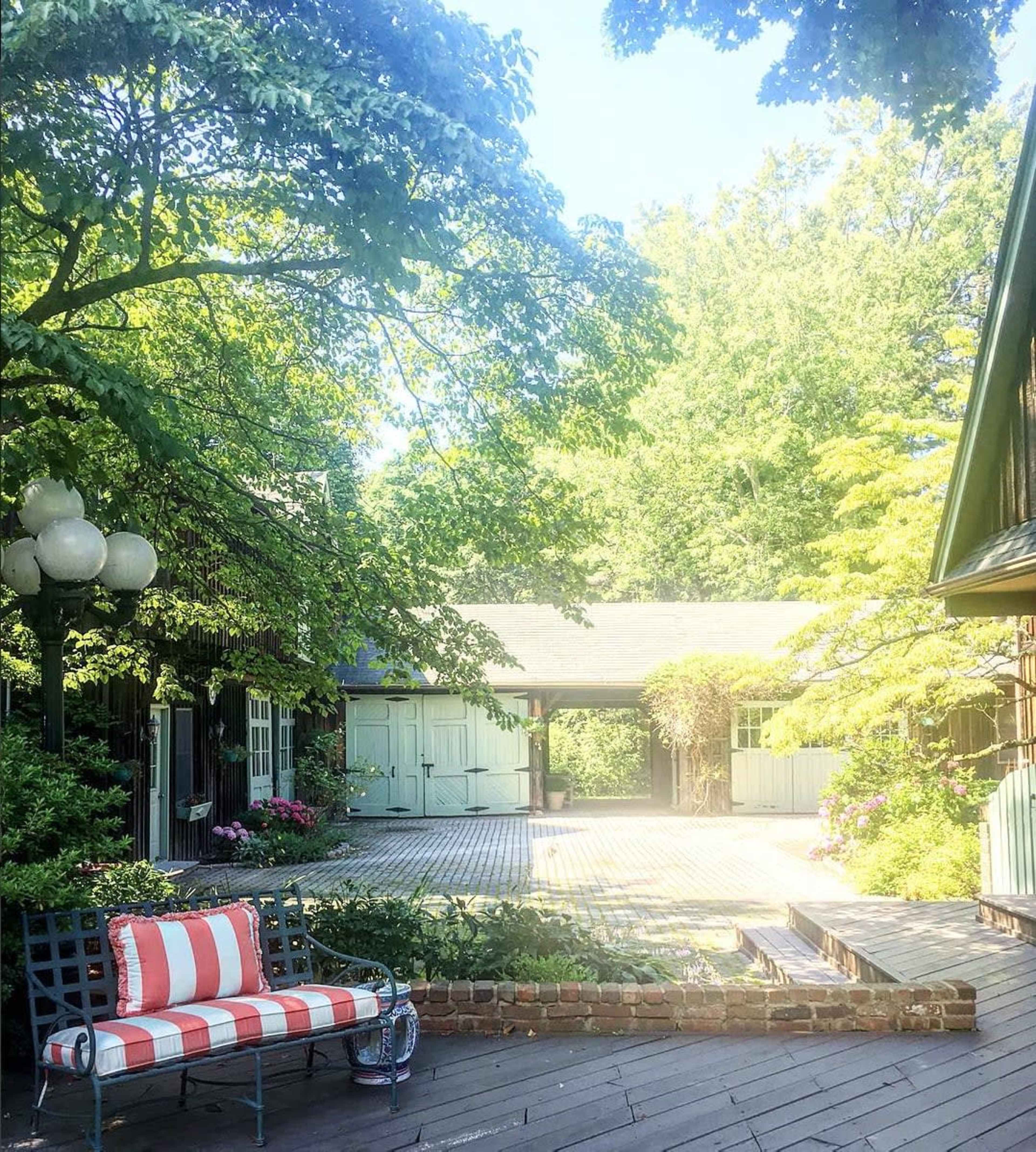 A patio area features a striped bench and is surrounded by lush greenery and blooming flowers.