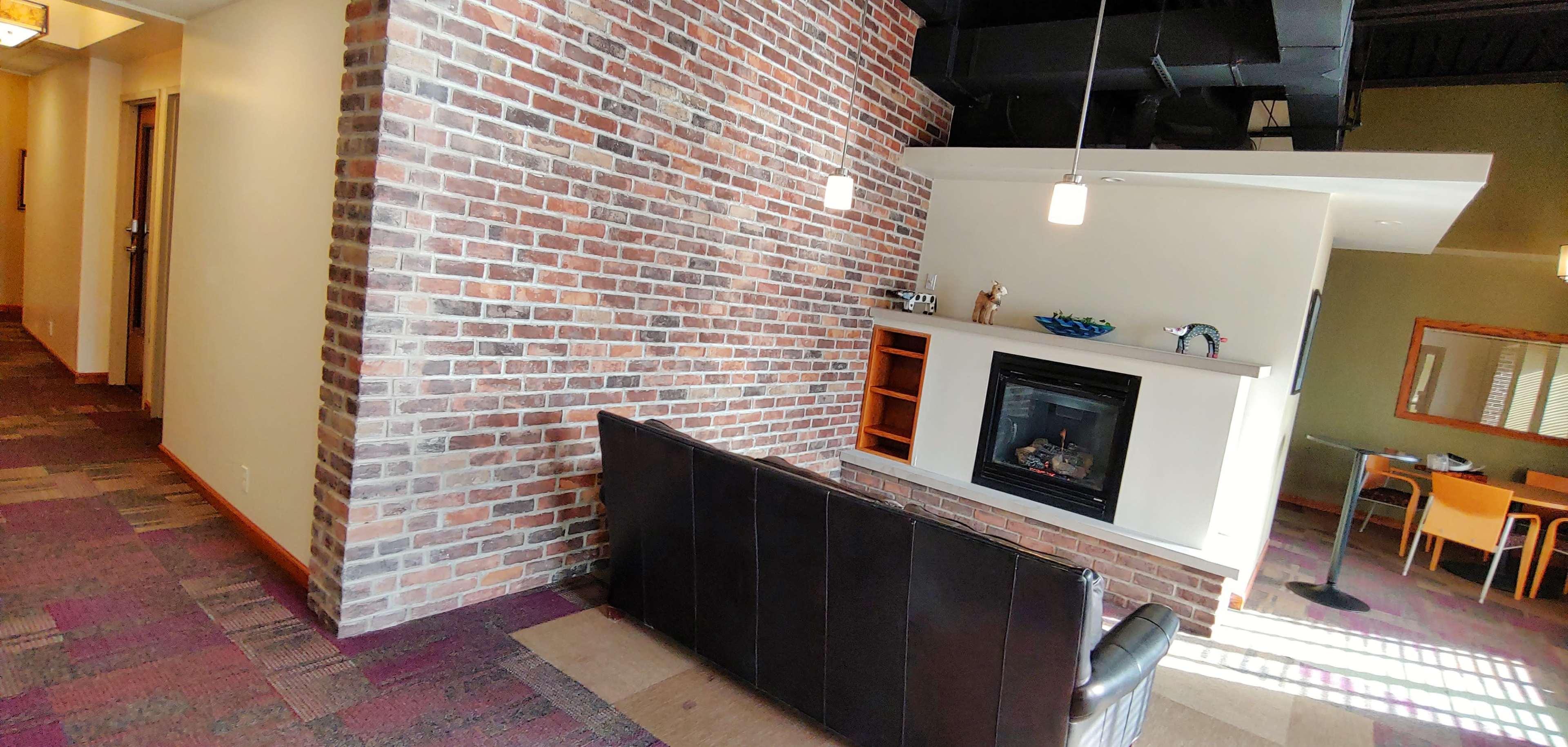 A lounge area featuring a brick accent wall, a fireplace with a shelf above it, and a sofa facing the fireplace.