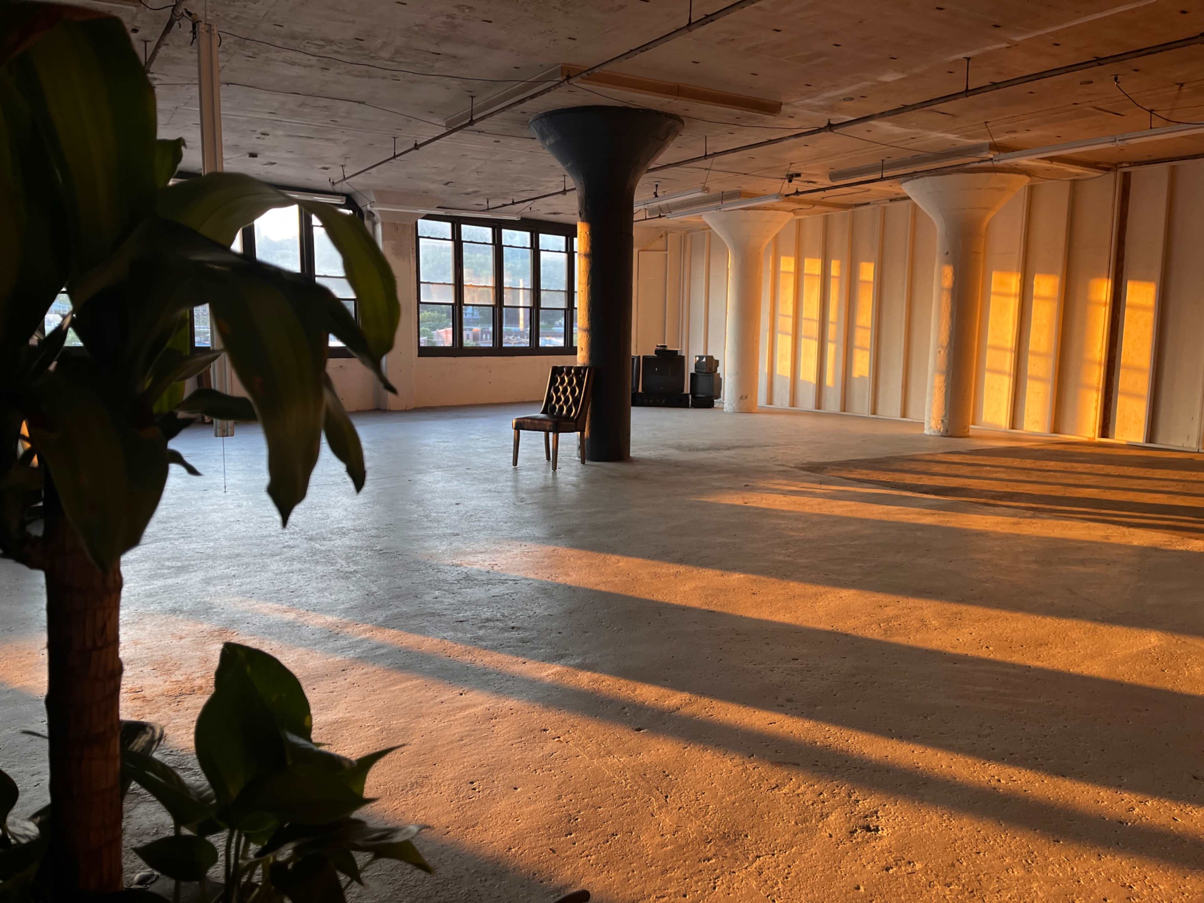 An empty industrial space with a single chair and long shadows cast by the setting sun through large windows.