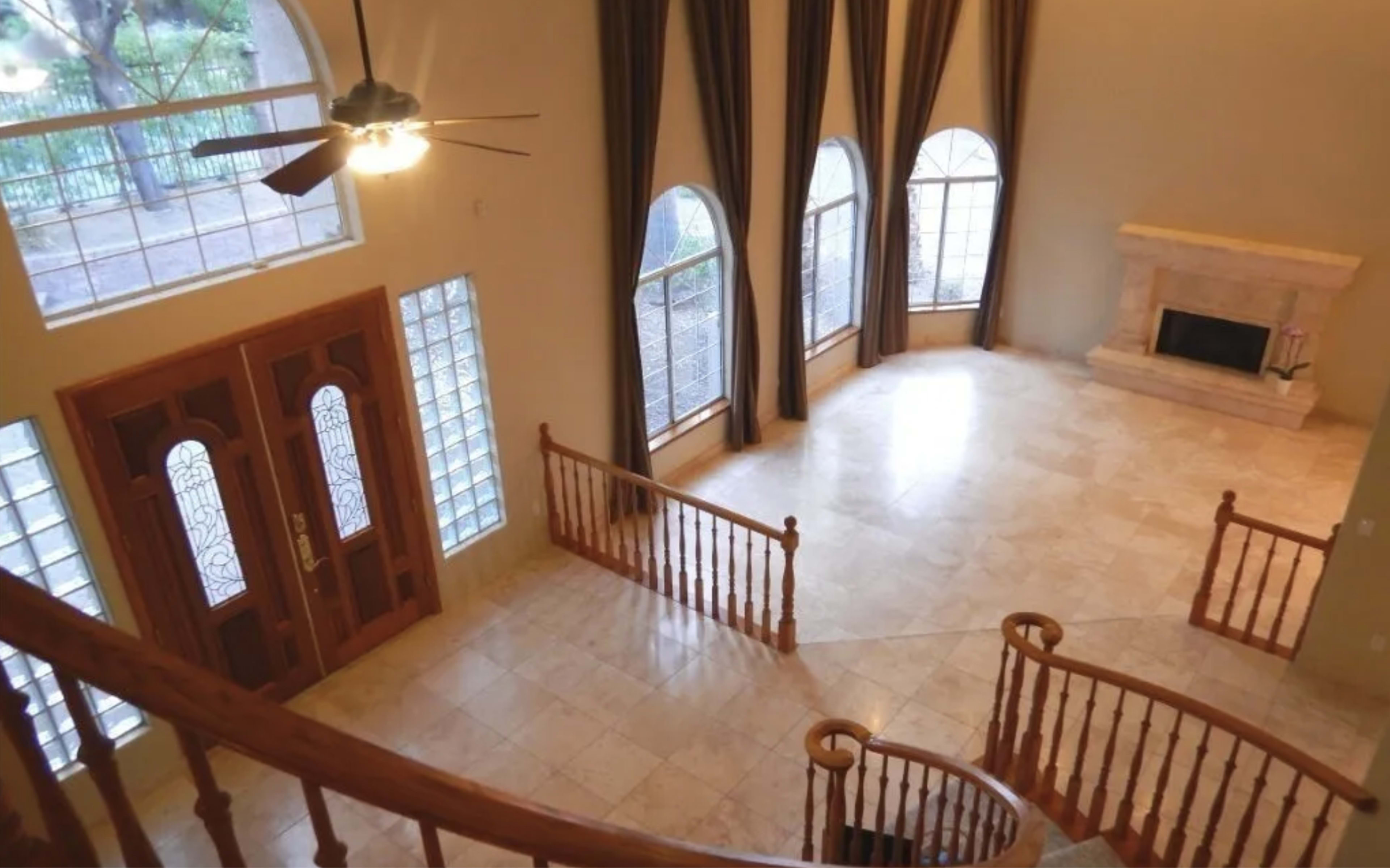 A spacious, empty living area with large arched windows, a stone fireplace, and a curved staircase.