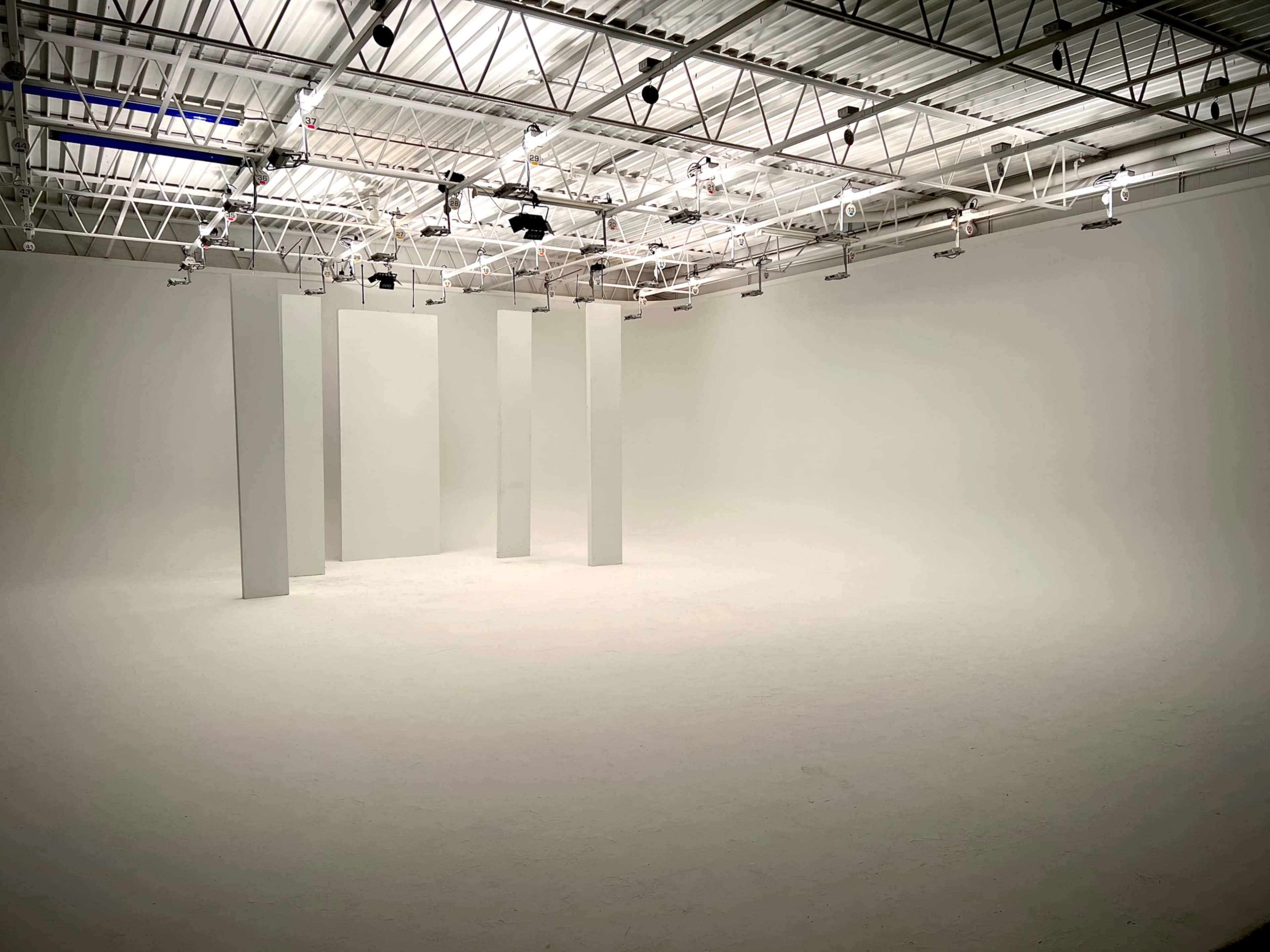 A spacious, empty studio with white walls and several vertical white columns spaced throughout the room.