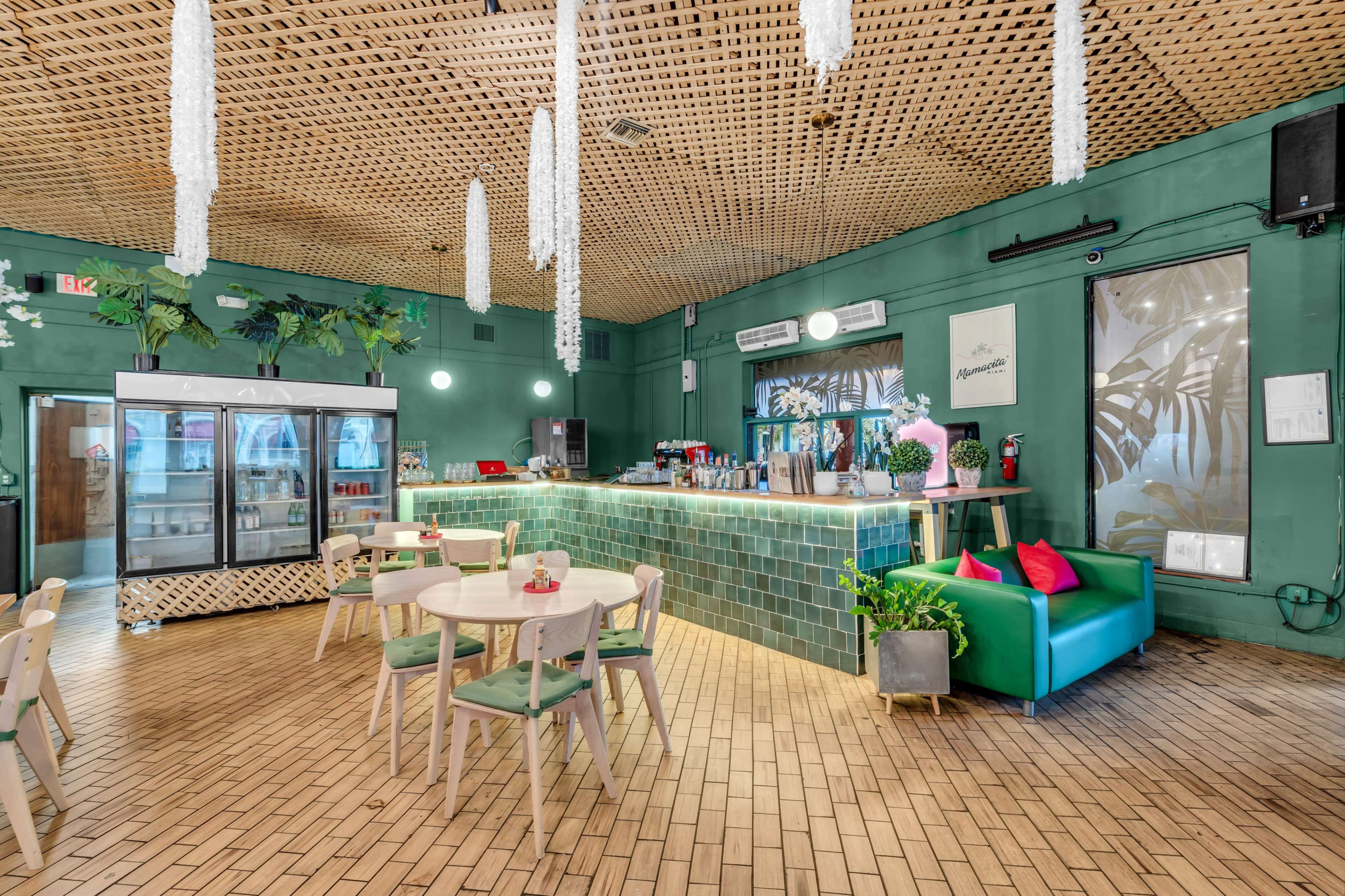 The image shows a modern café interior with green walls, wooden ceiling, a tiled bar area, and seating arrangements including tables and chairs.