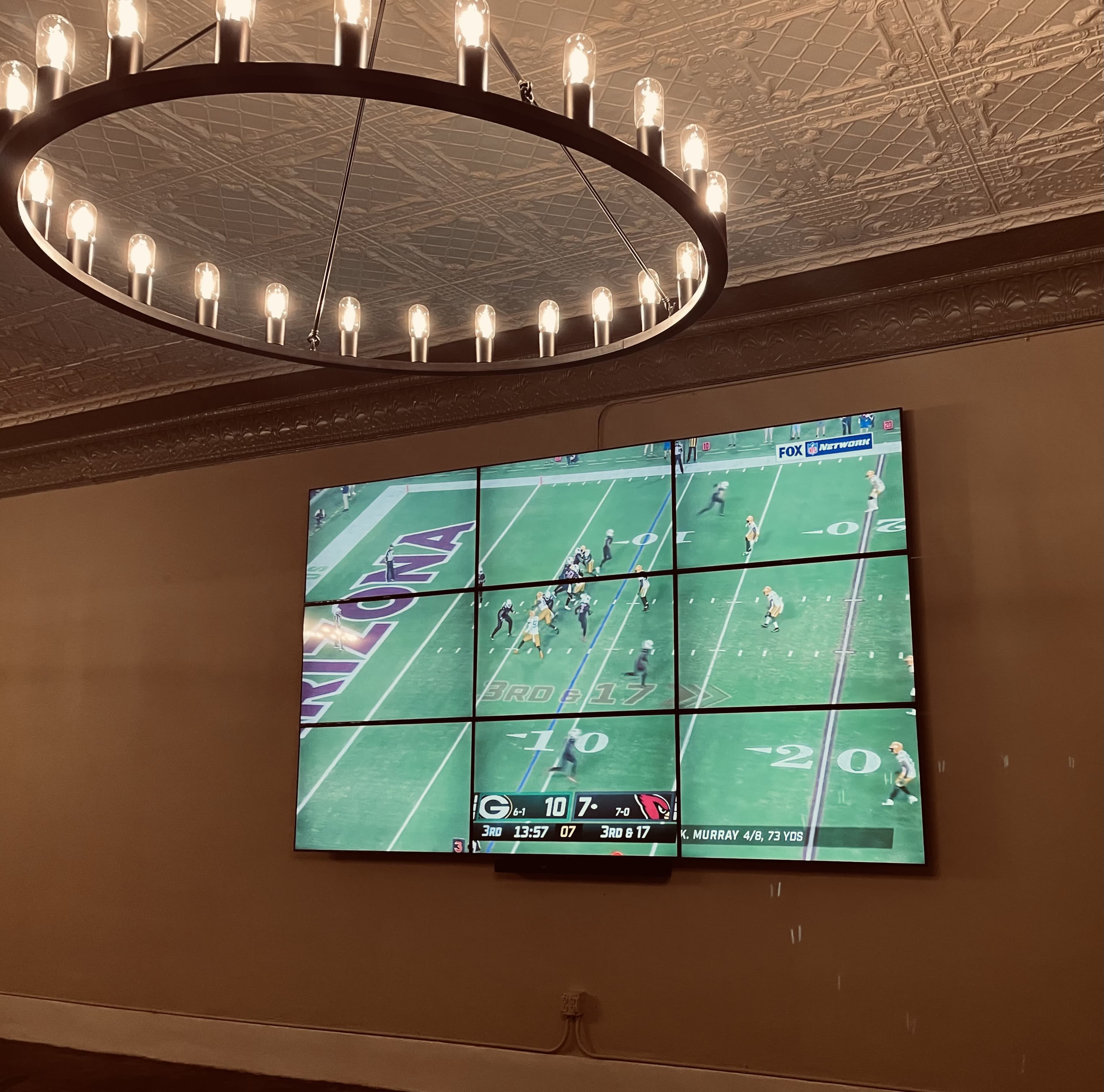 A large TV screen displaying a football game is mounted on the wall under a circular light fixture.