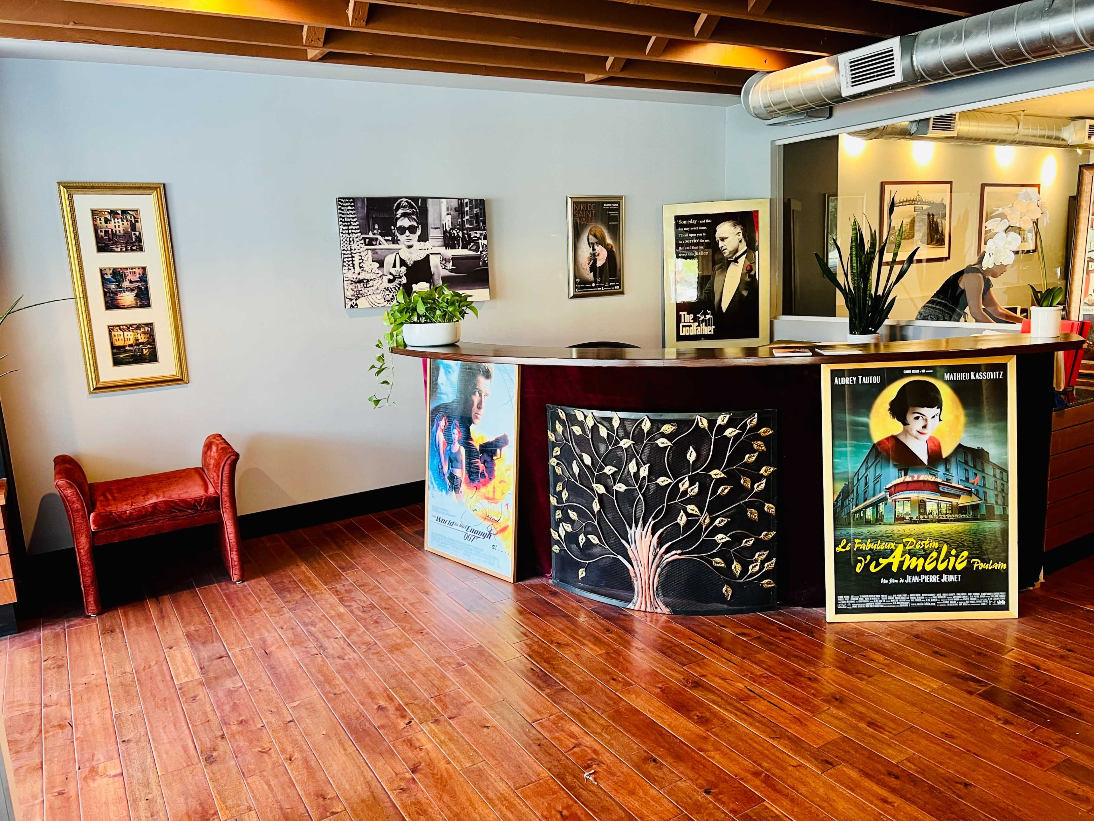 A reception area featuring a wooden counter decorated with a tree design, framed posters, black-and-white photographs on the walls, and a red chair in the corner.