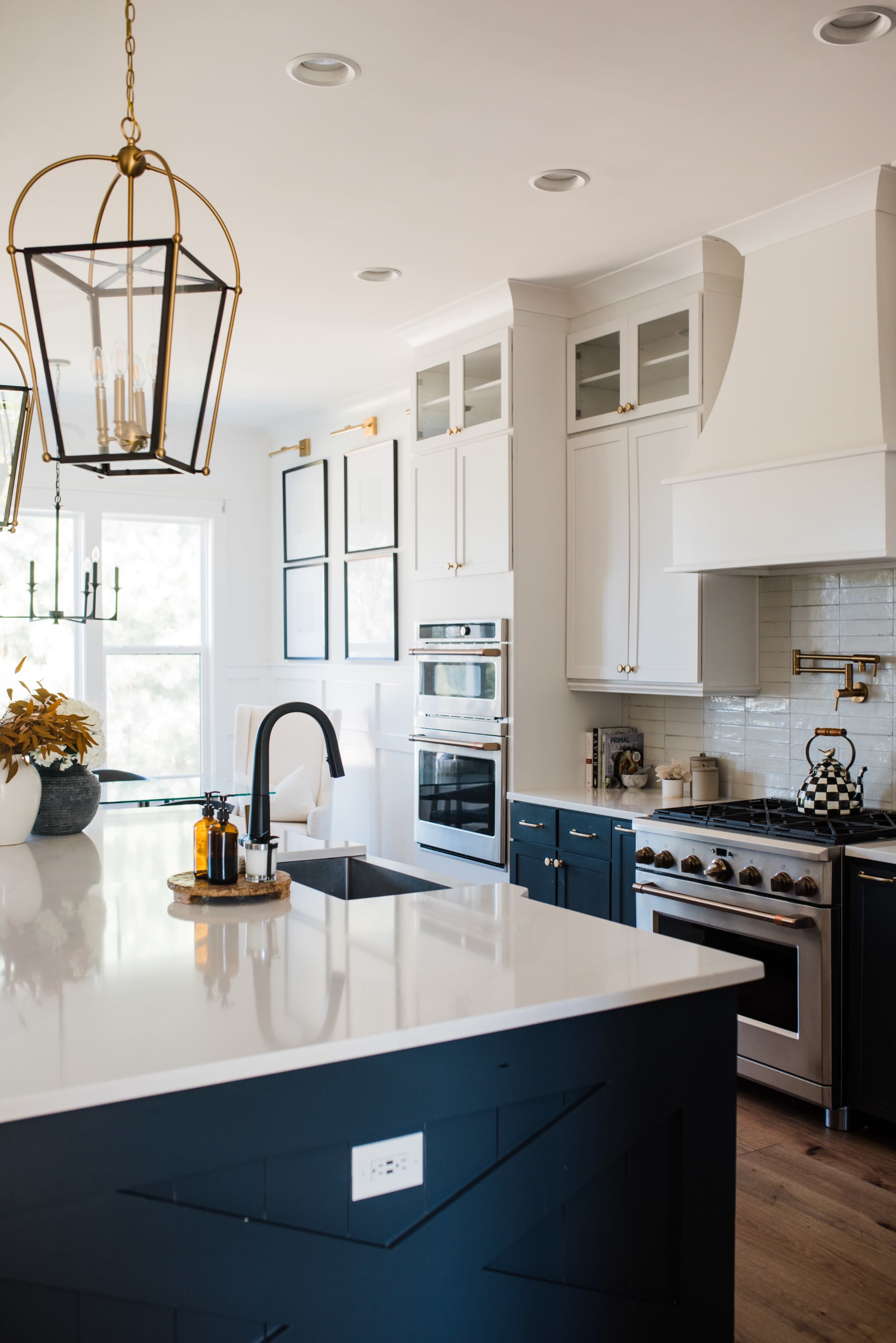 A modern kitchen featuring a central island with a dark blue base, white countertops, and stainless steel appliances, complemented by pendant lighting and cabinetry.