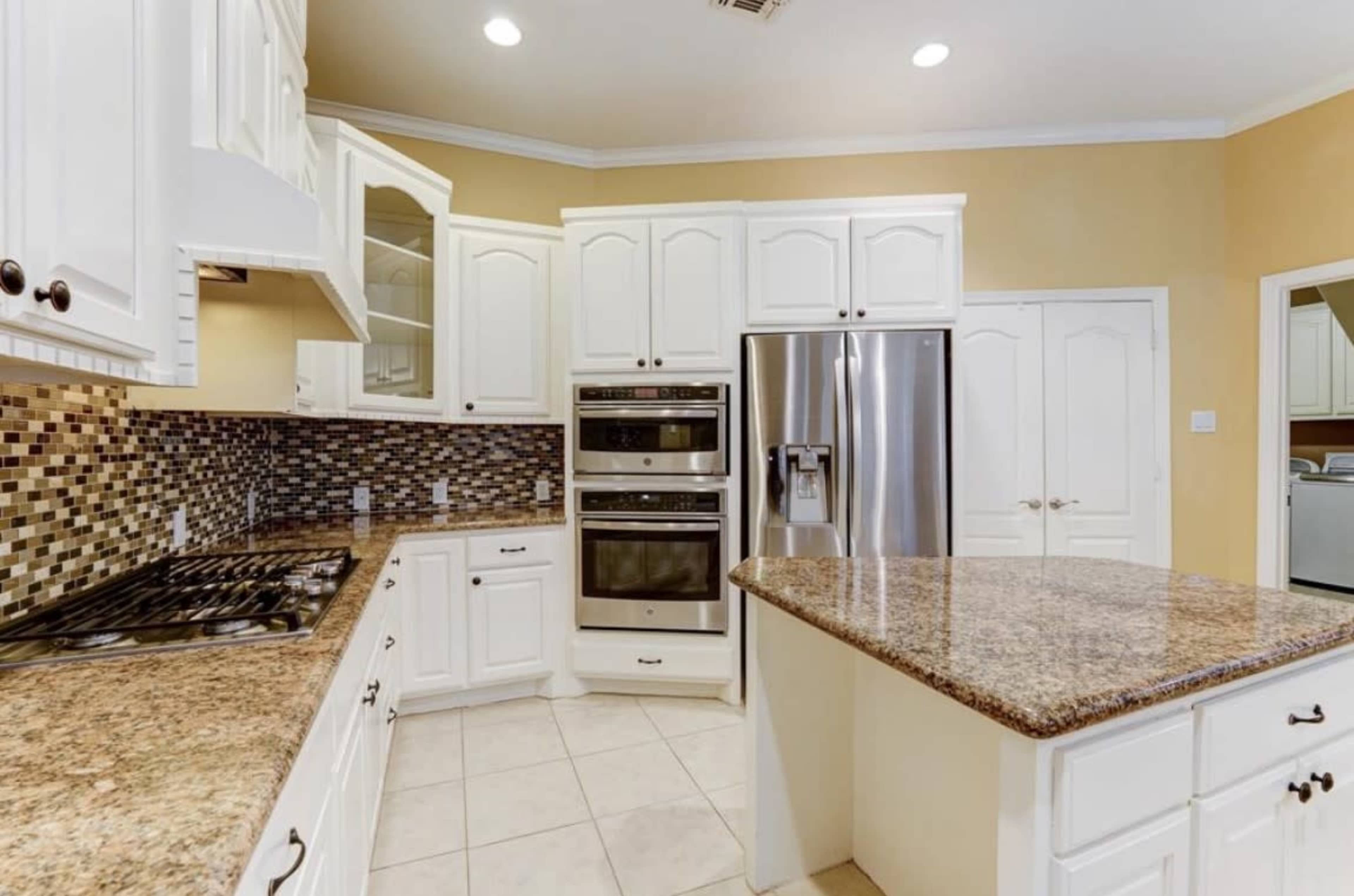 The kitchen features white cabinetry, stainless steel appliances, and a granite countertop with a mosaic tile backsplash.