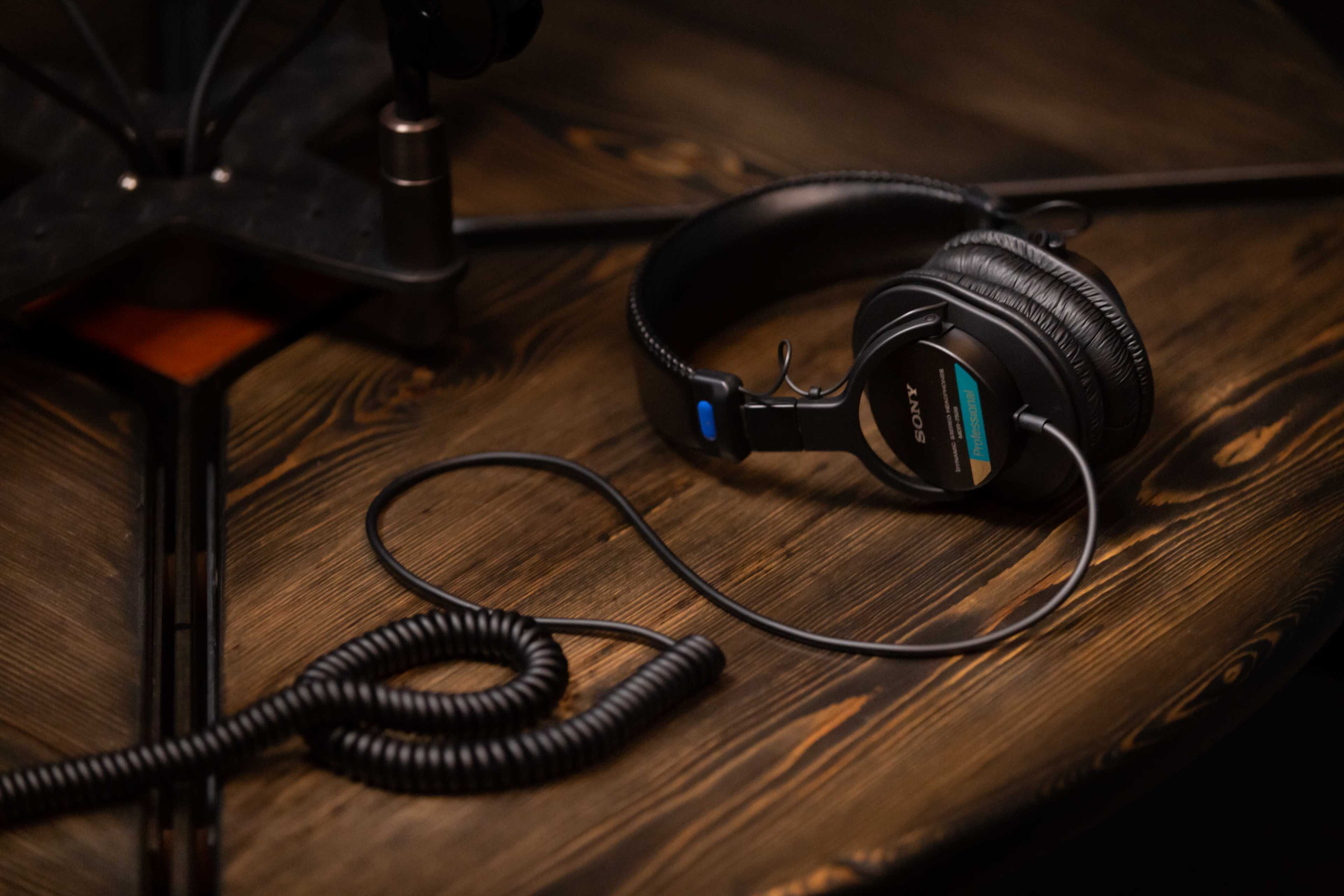 A pair of black Sony headphones rests on a wooden table, connected by a coiled cable.