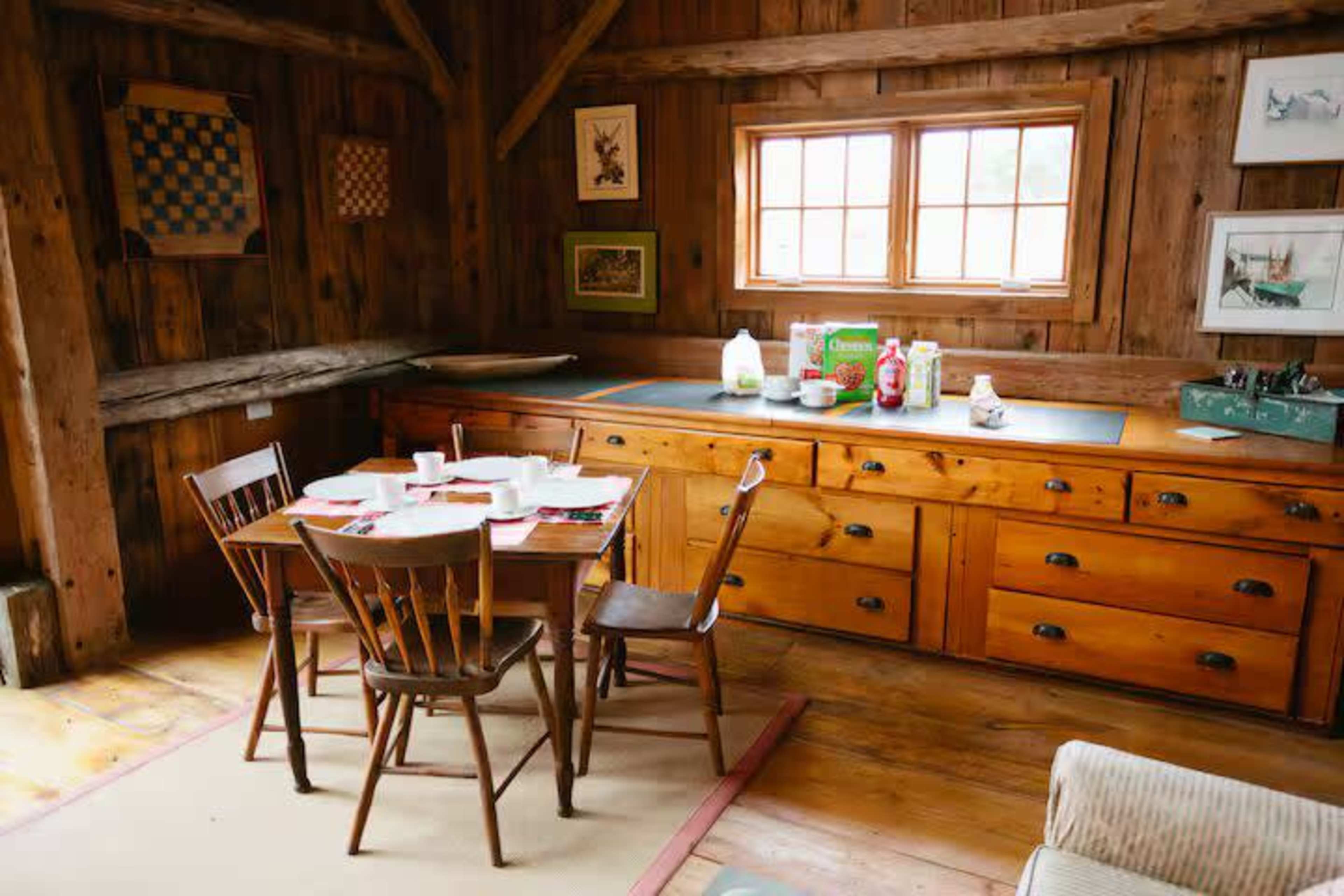 The image shows a cozy wooden kitchen with a table set for a meal and various items, including condiments and milk, displayed on the countertop.