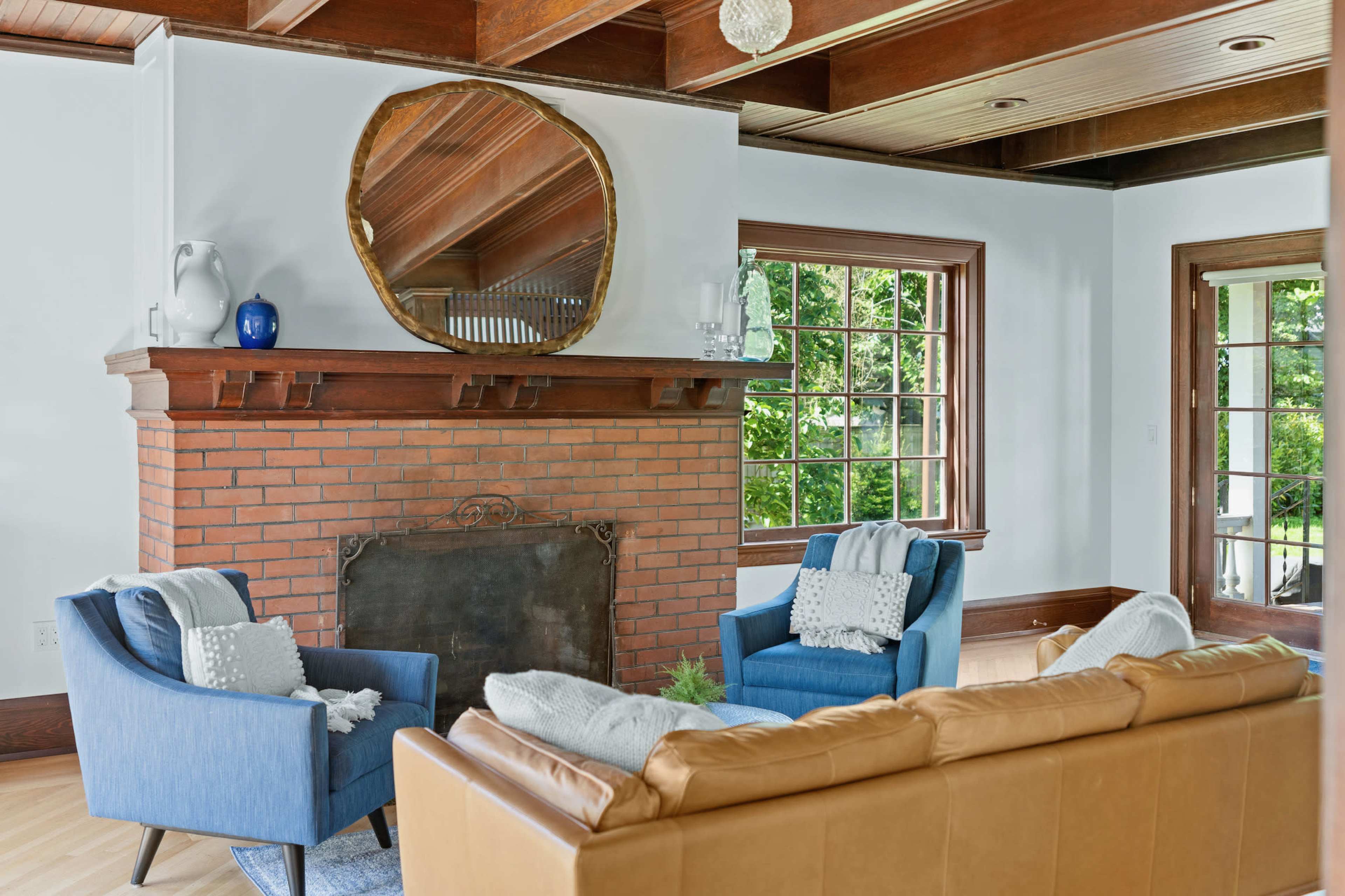 A living room features a brick fireplace with a round mirror above it, flanked by two blue armchairs and a brown sofa.