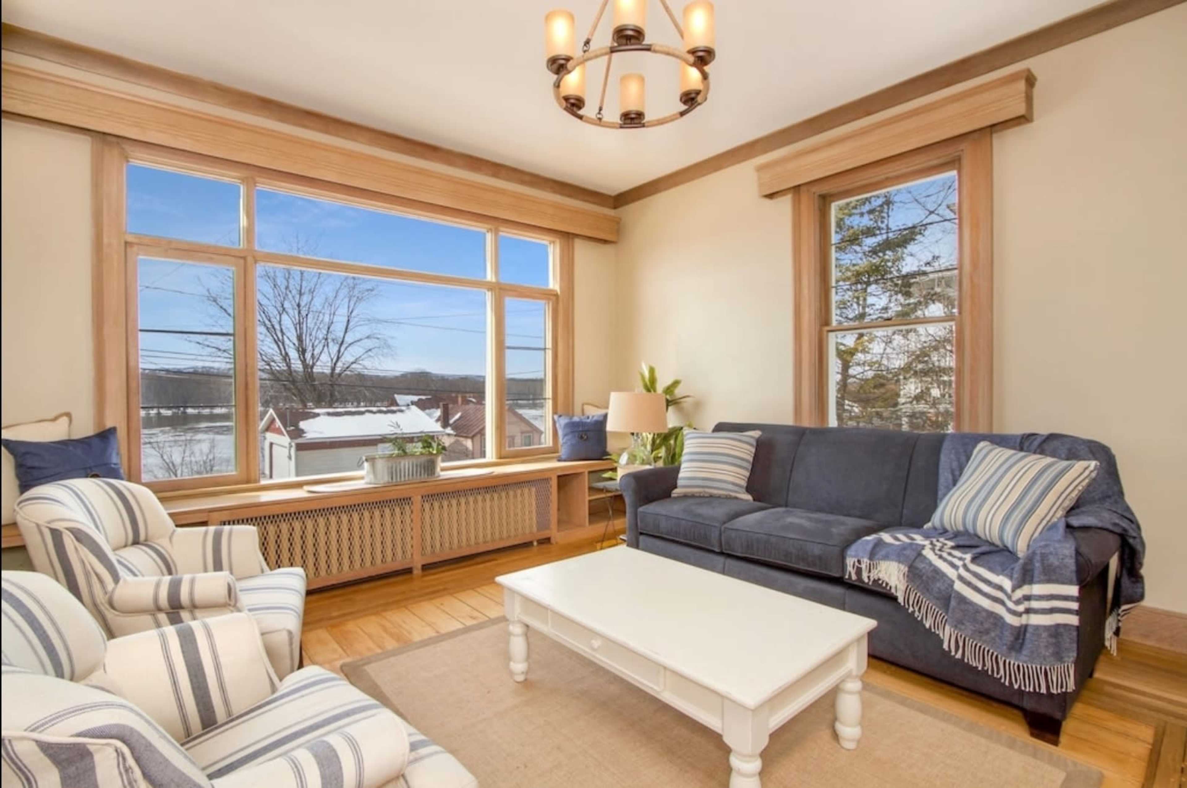 A living room with large windows overlooking a snowy landscape, featuring a blue sofa, striped armchairs, and a white coffee table.