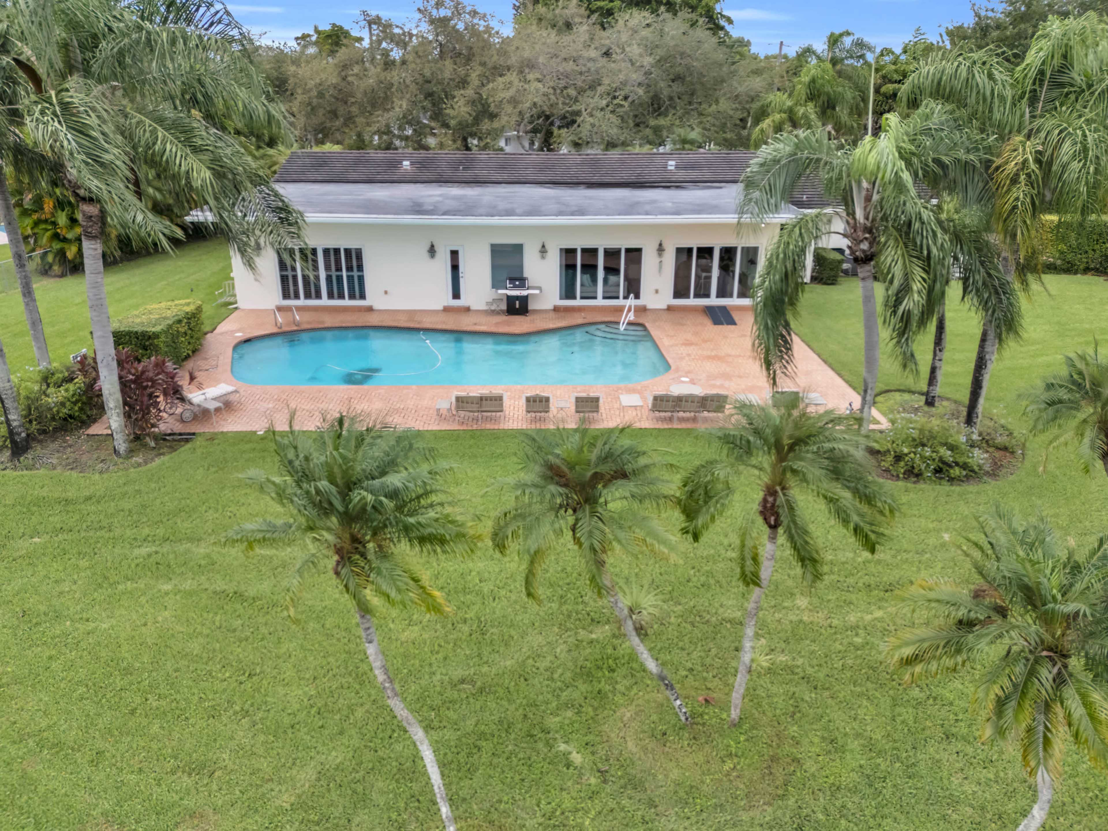 A house with a swimming pool surrounded by palm trees is visible in a landscaped yard.