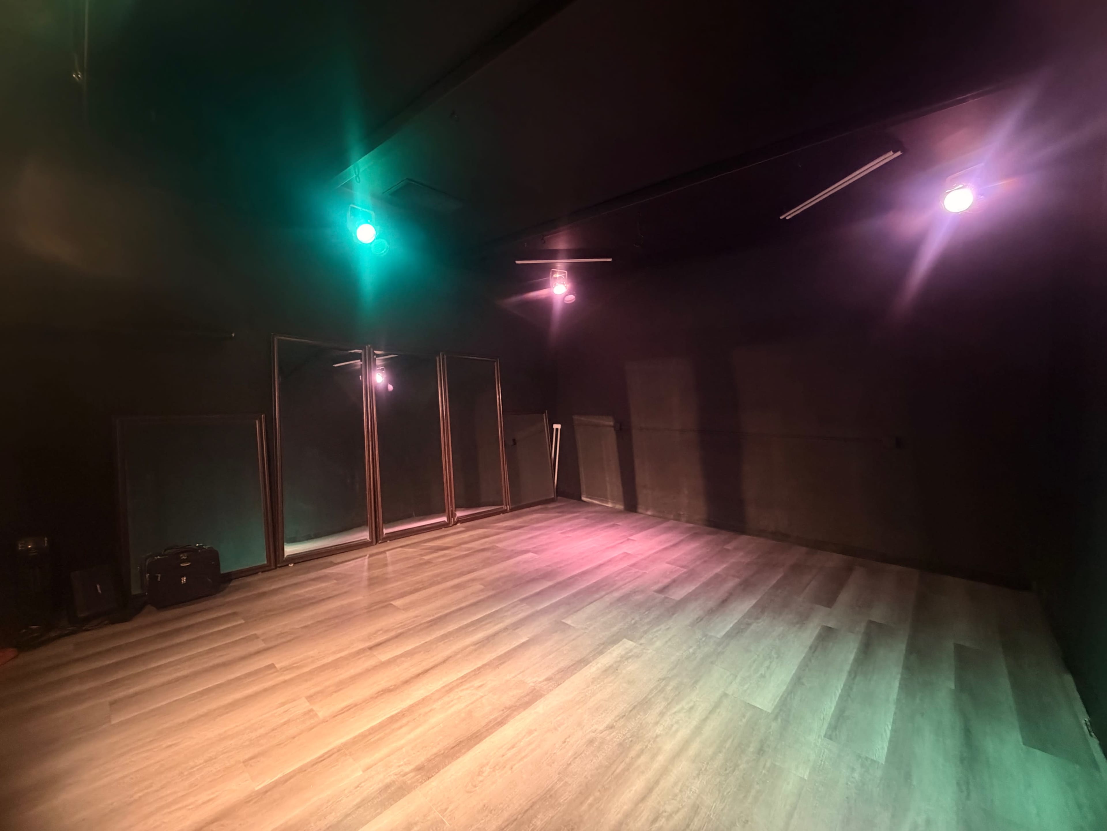 The image shows an empty dance studio with mirrored walls and colored ceiling lights illuminating the wooden floor.