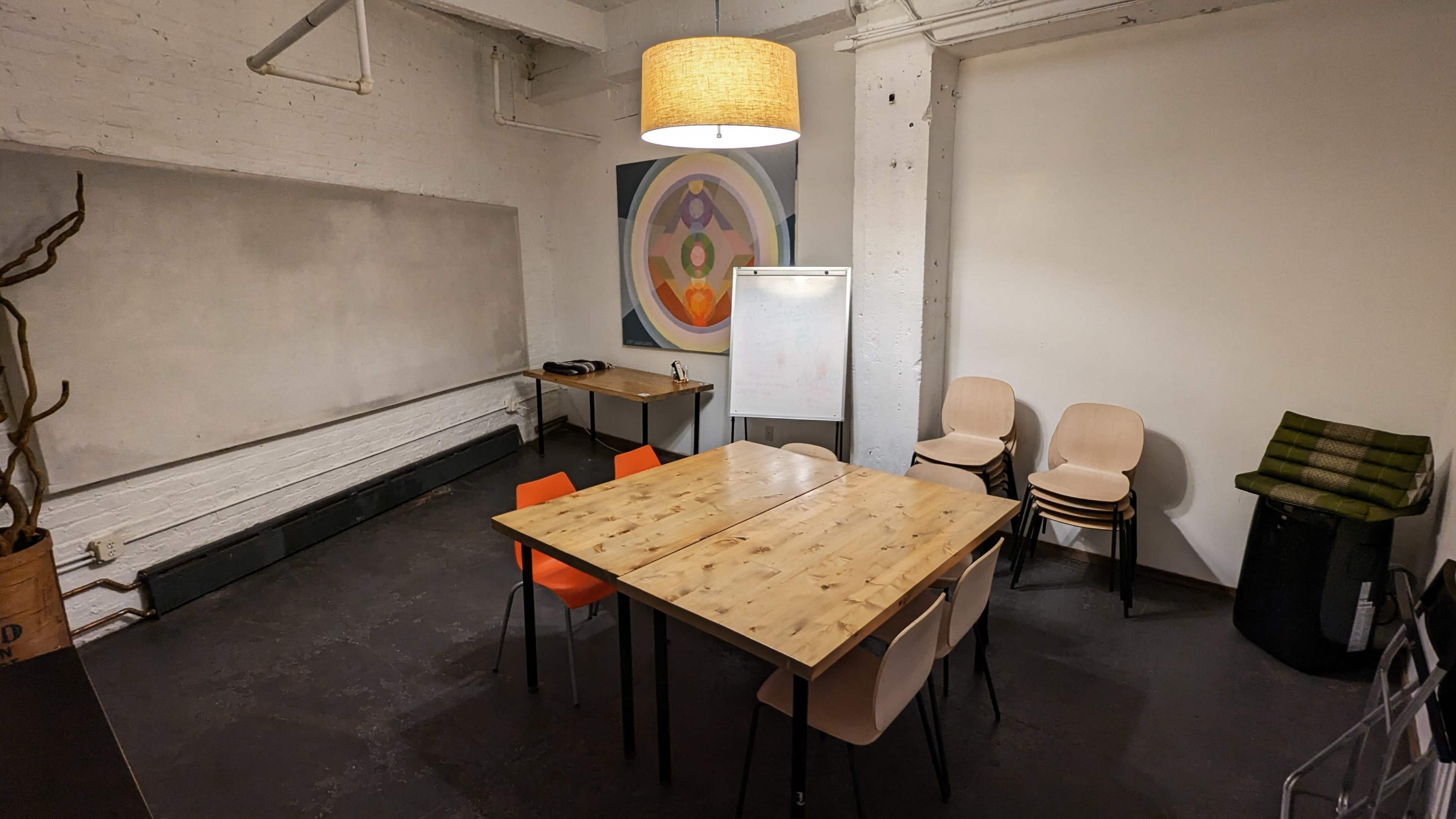 A meeting room featuring a wooden table surrounded by chairs, a whiteboard, and a lamp hanging from the ceiling.