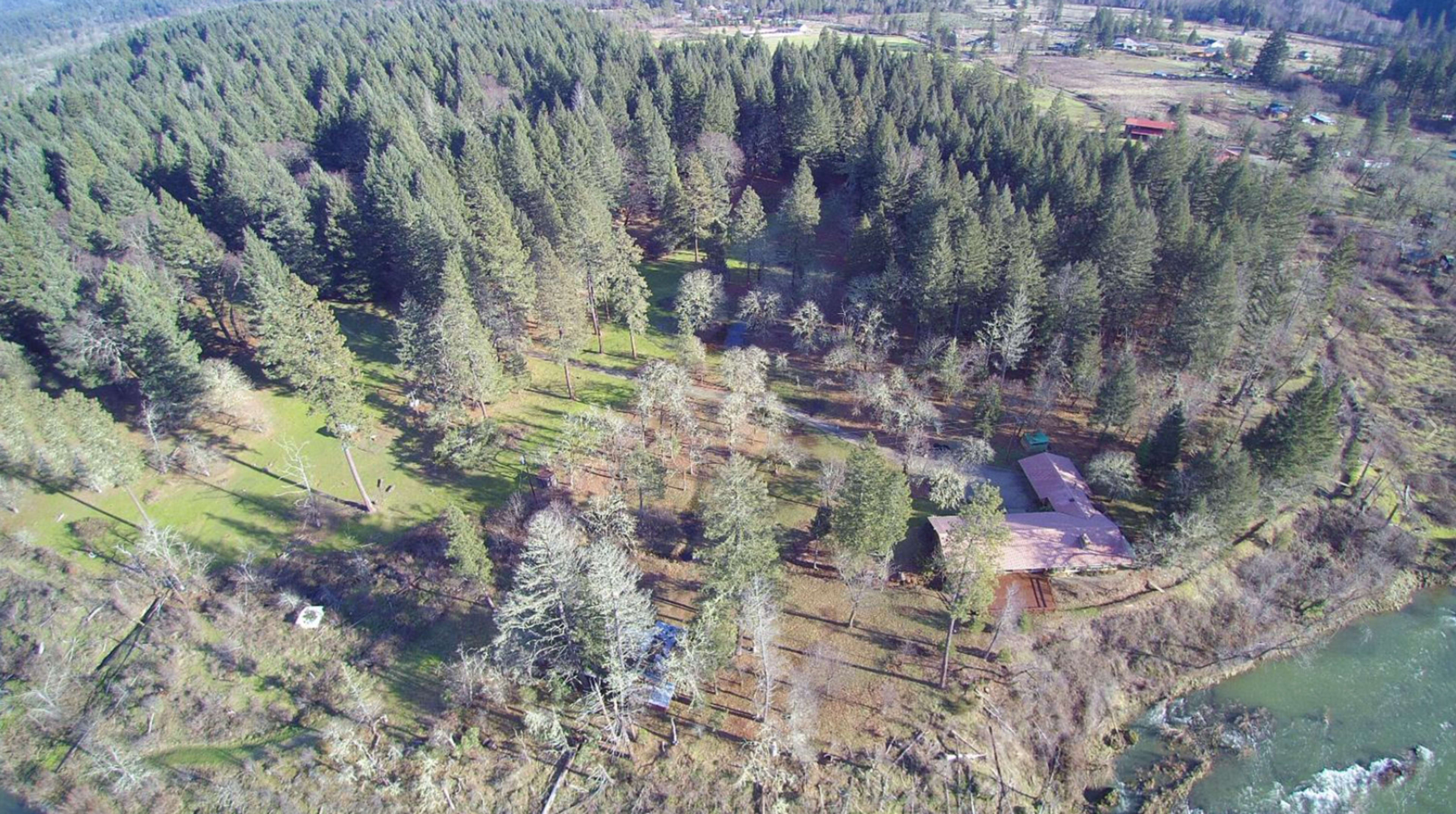 An aerial view shows a densely forested area with a river and a small building nestled among the trees.