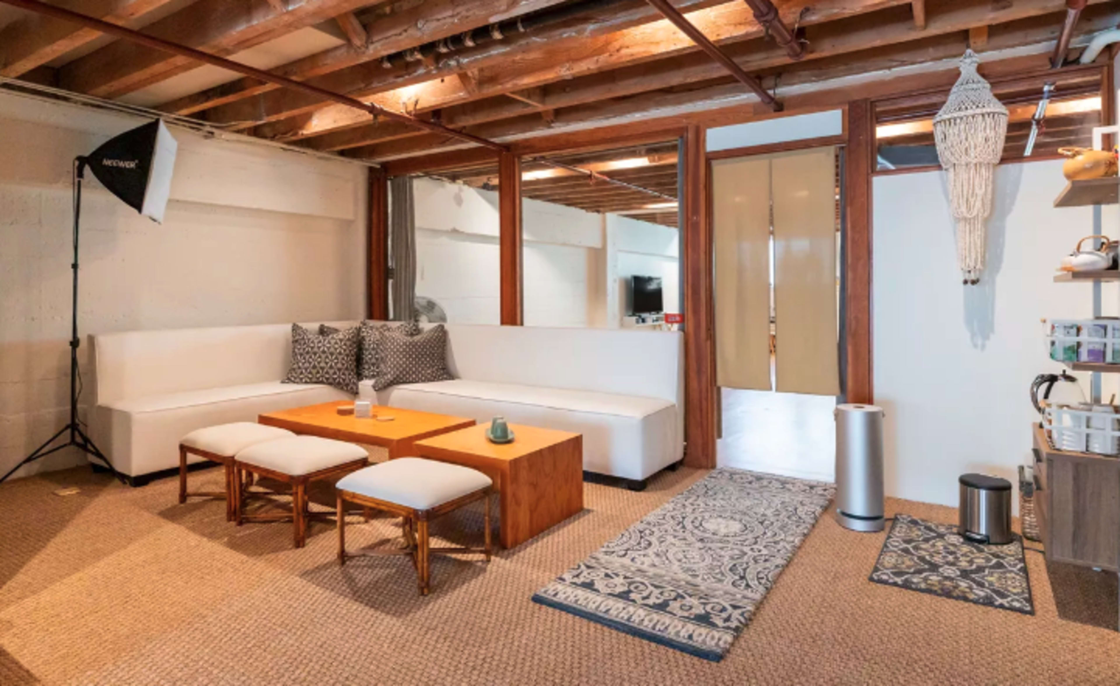 A minimalist living room with a white sectional sofa, a wooden coffee table, and patterned rugs on a textured floor.