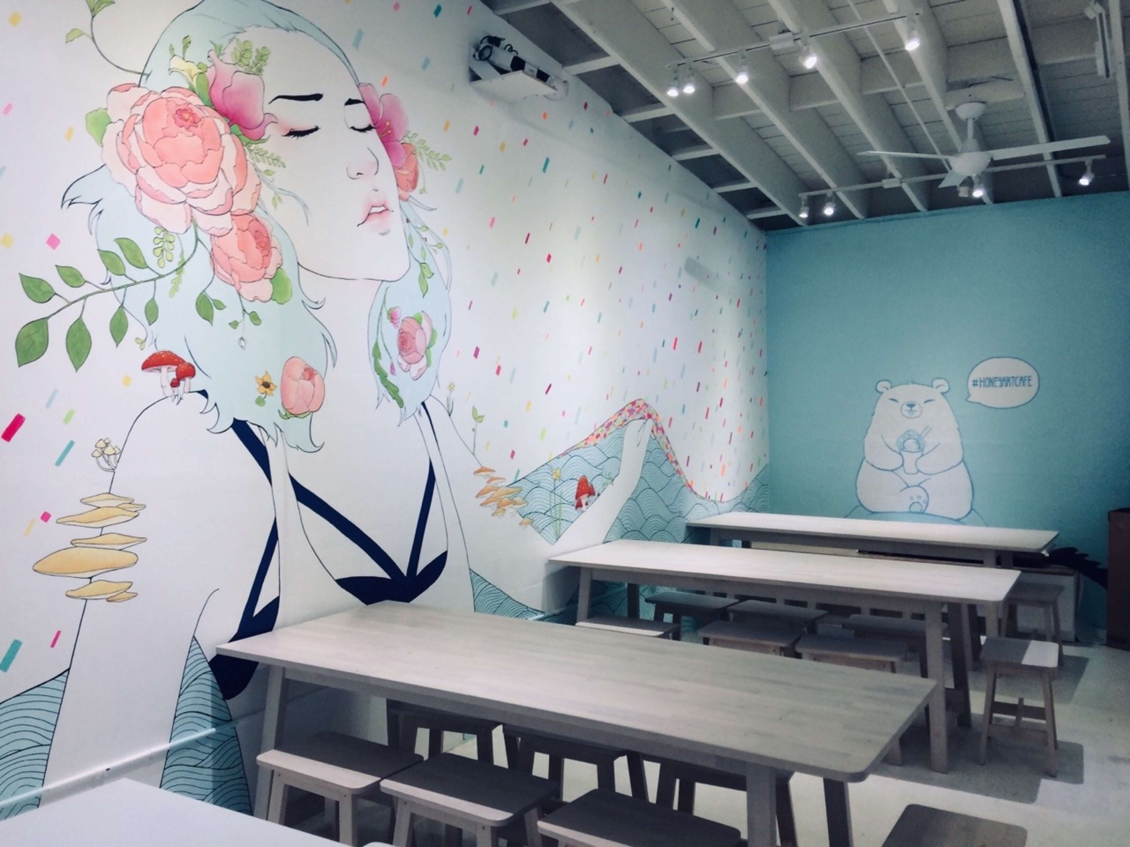 A brightly decorated café with large wall murals featuring a woman surrounded by flowers and a bear, complemented by wooden tables and chairs.