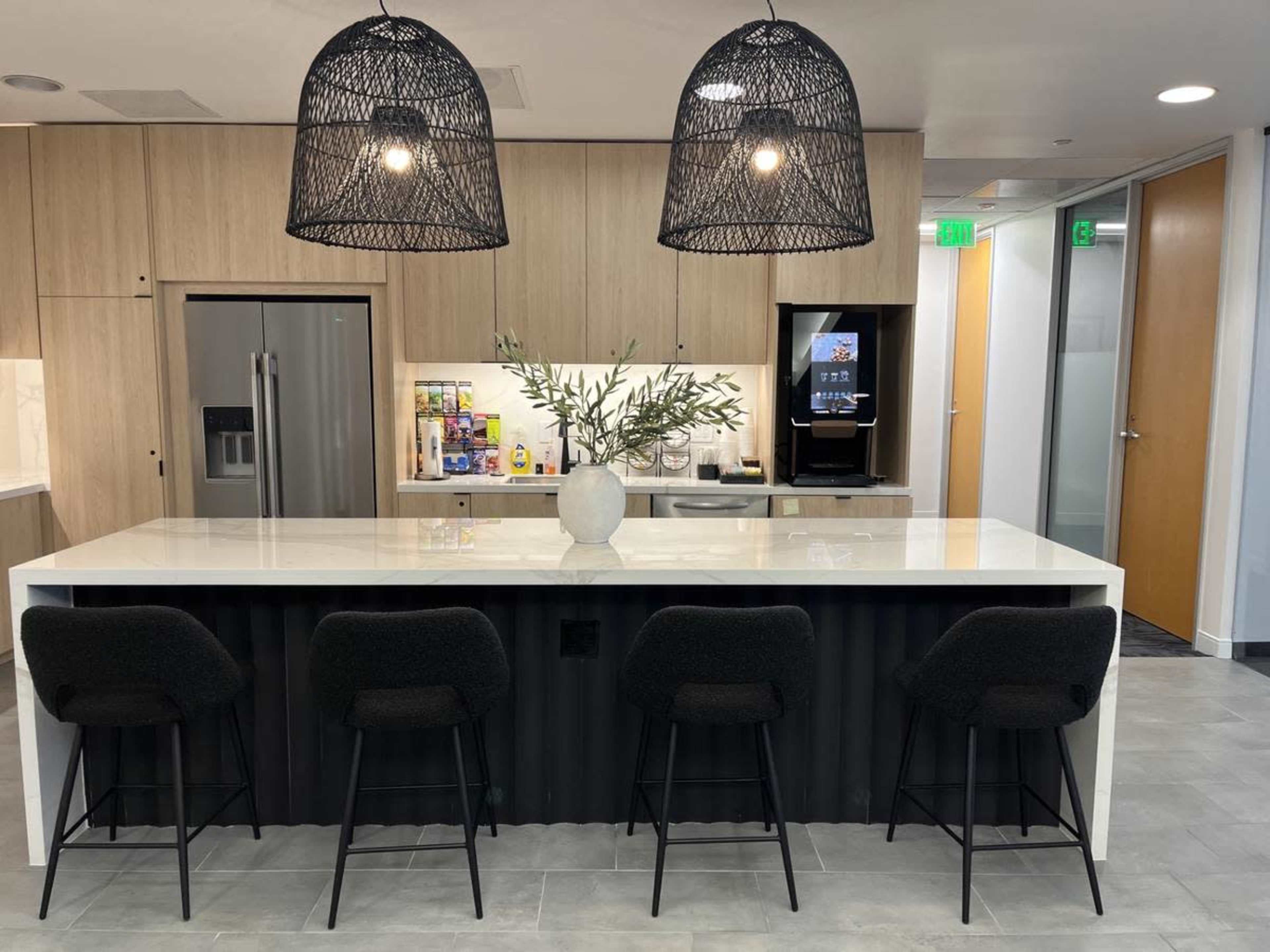 The image shows a modern kitchen area with a large white countertop island, four black bar stools, and pendant lighting above.