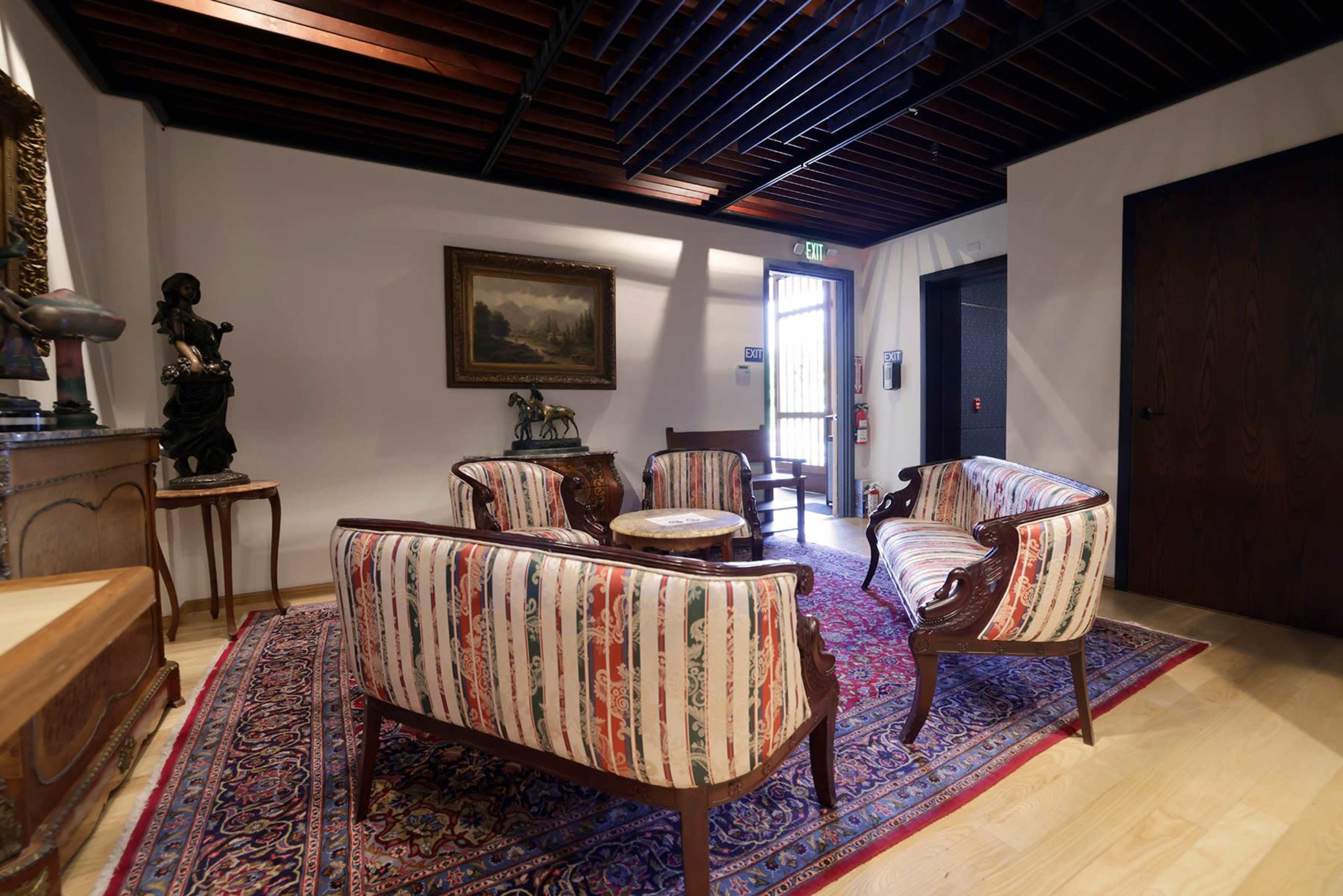 The image shows a corner of a room with four upholstered chairs arranged around a small table on a patterned rug, accompanied by a decorative statue and artwork on the walls.