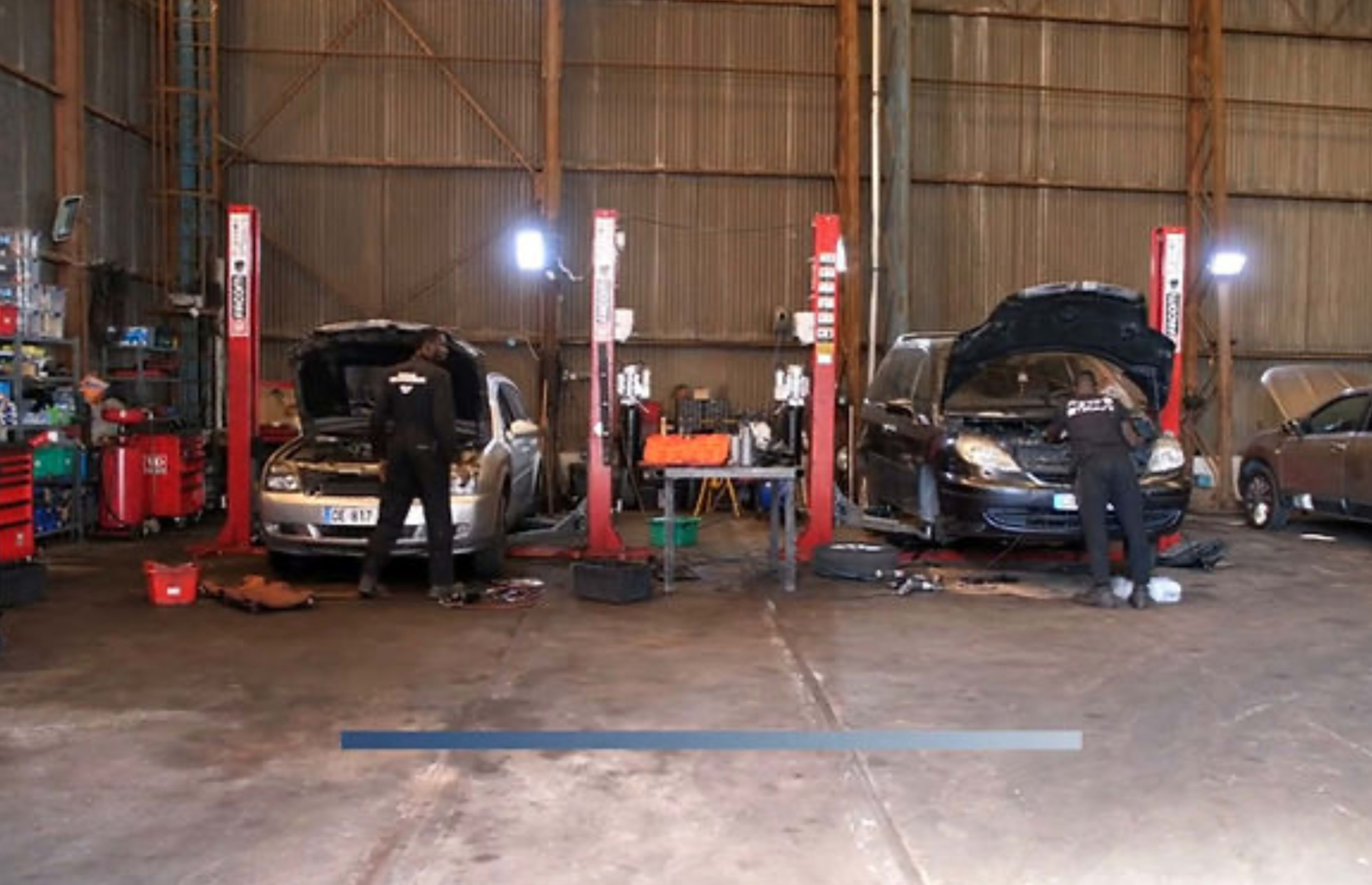 Two mechanics work on cars positioned on hydraulic lifts in an automotive repair shop.