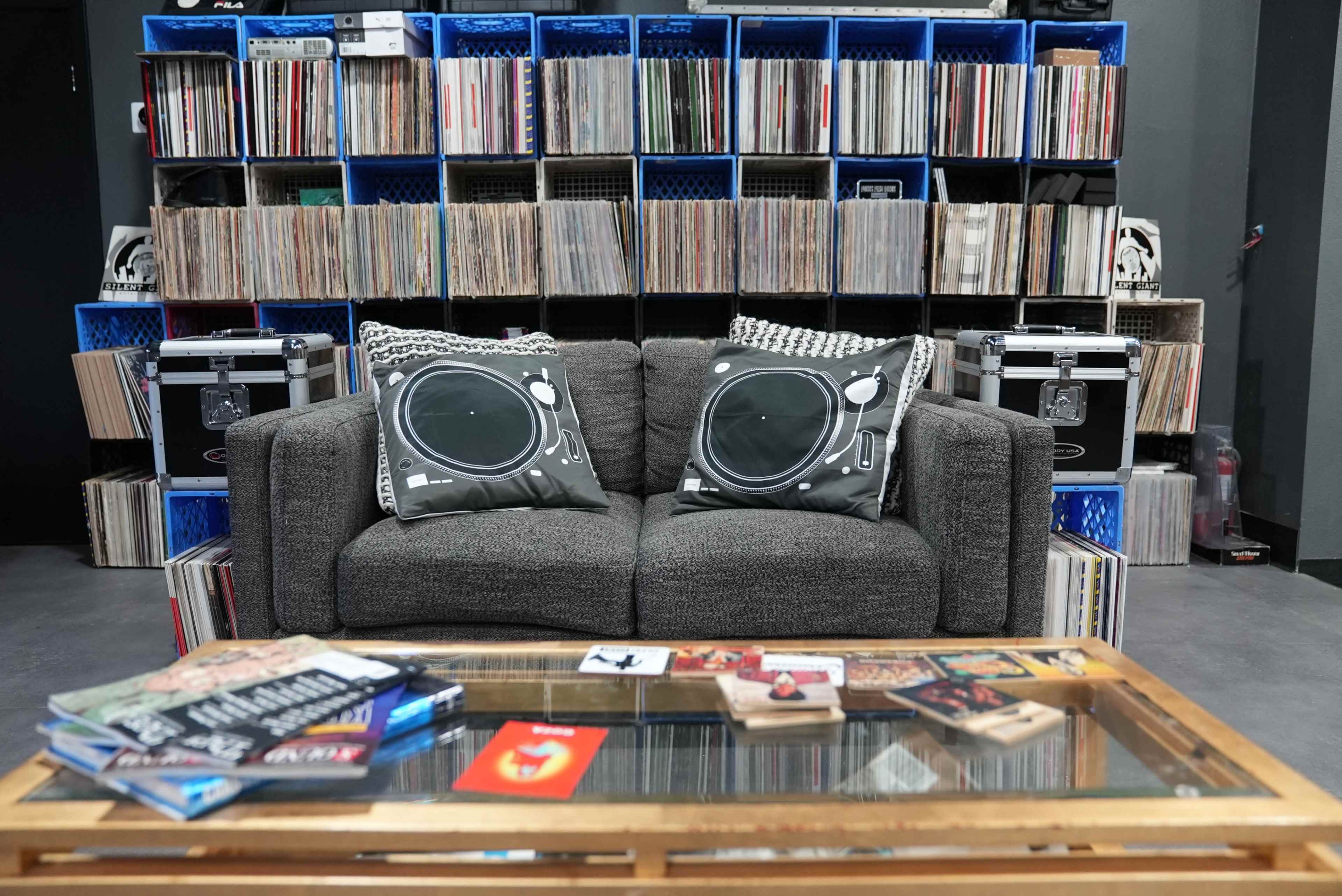 A gray couch with turntable-patterned cushions sits in front of a wall of vinyl records organized on shelves.