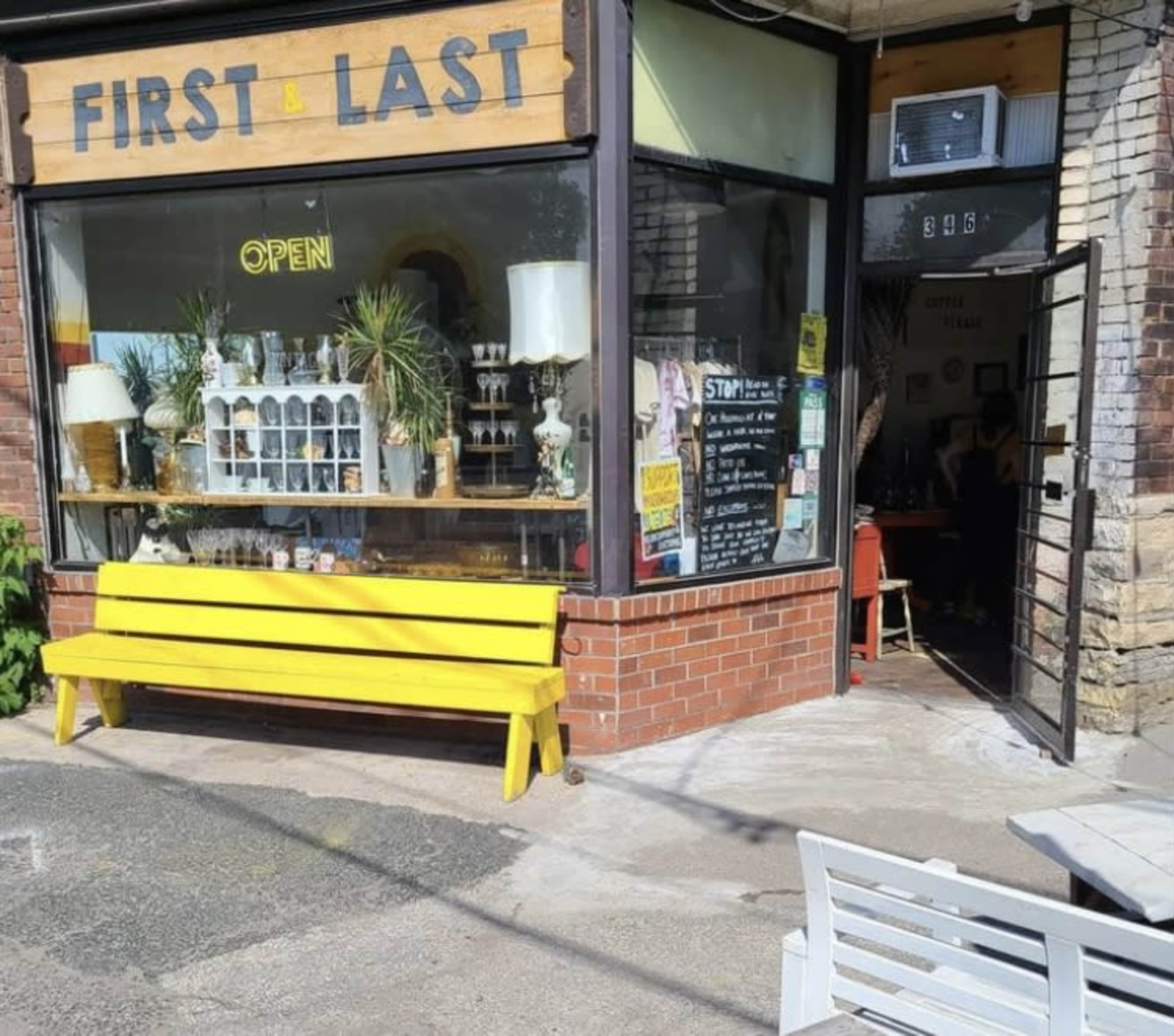 The exterior of a store named "FIRST & LAST," featuring large windows displaying various items and a bright yellow bench in front.