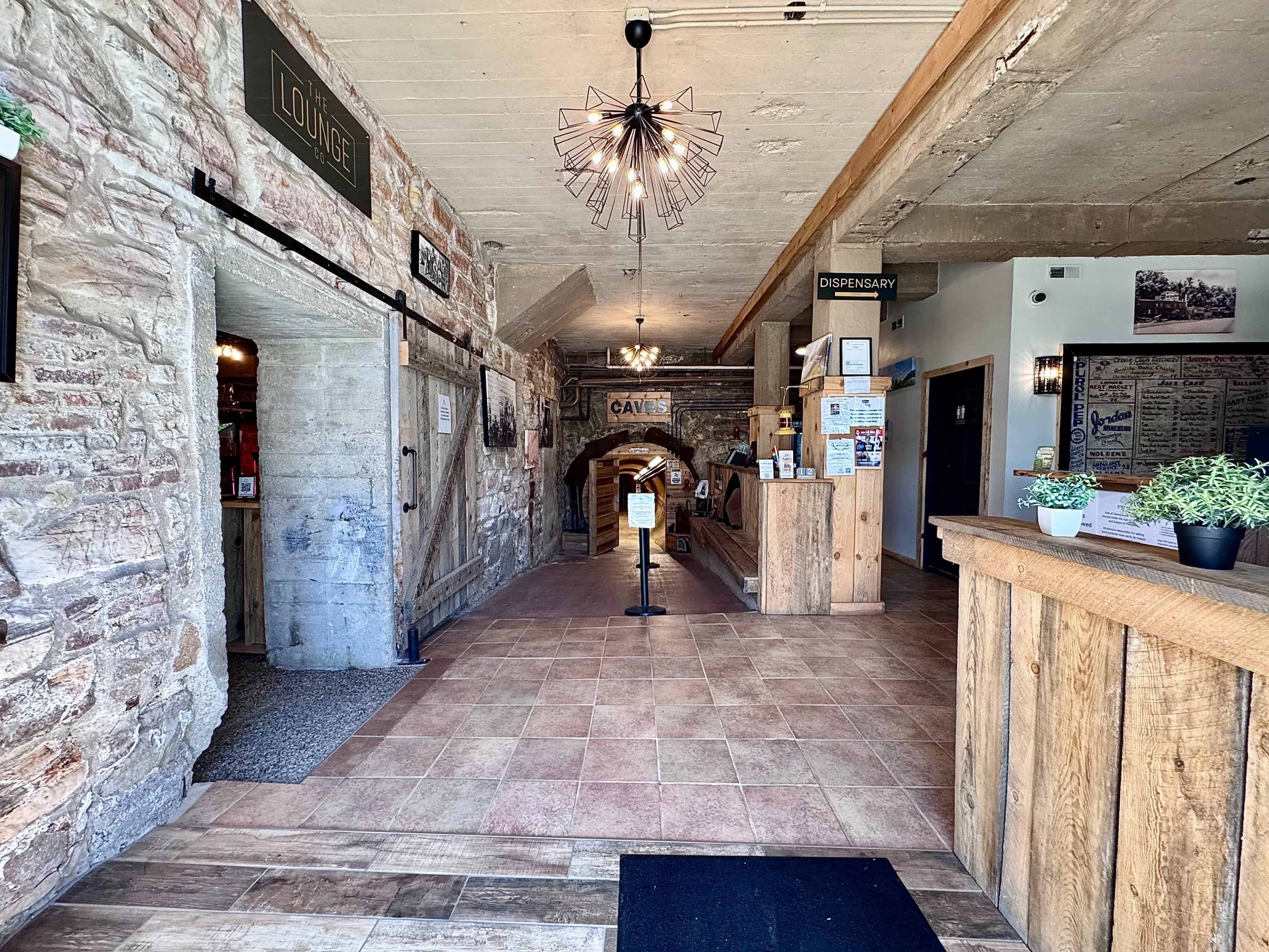 The image shows an interior entrance to a lodge with a stone wall on one side and a wooden reception area on the right.