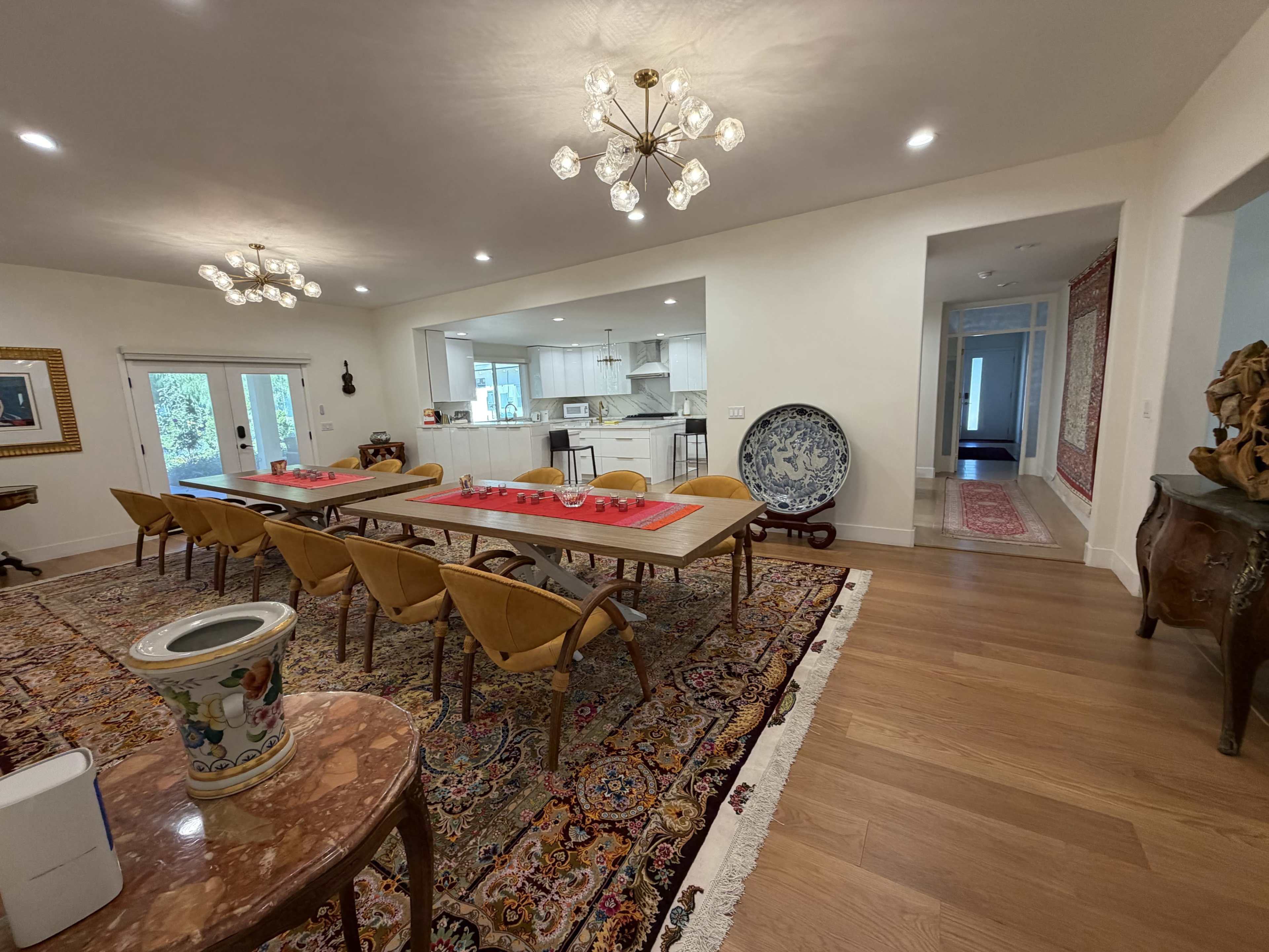 A spacious dining area features a long table surrounded by chairs, with a view of a nearby kitchen and hallway.