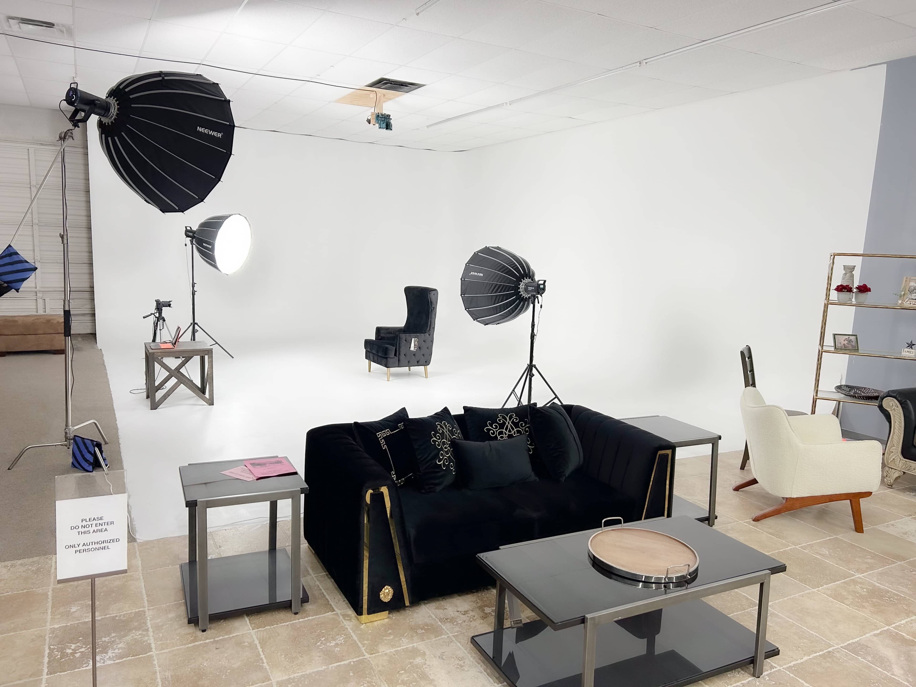 A photography studio featuring a black sofa, a chair, and various lighting equipment in front of a plain white backdrop.