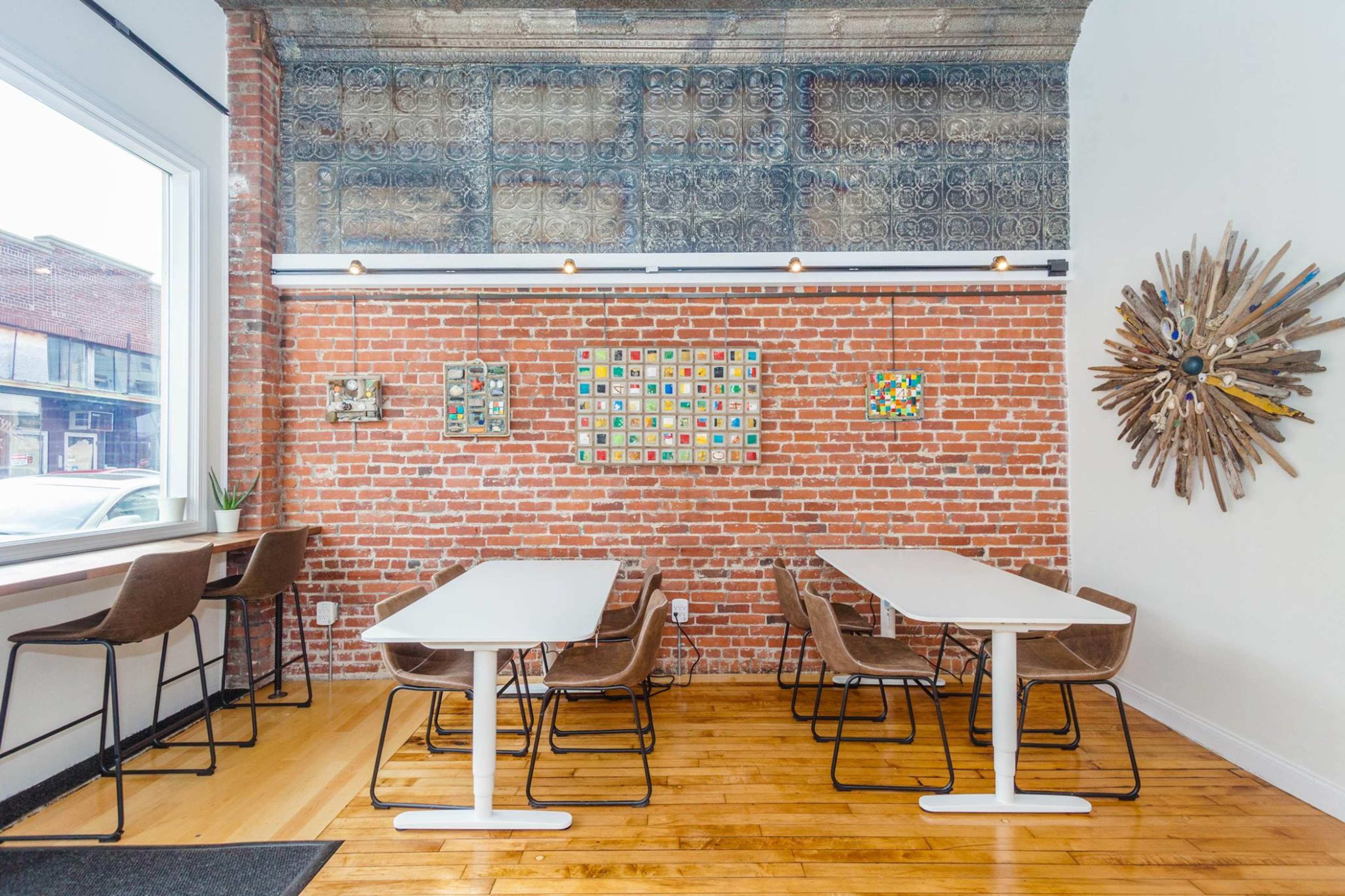 A cozy café interior featuring exposed brick walls, wooden floors, and a mix of tables and chairs arranged against the walls.