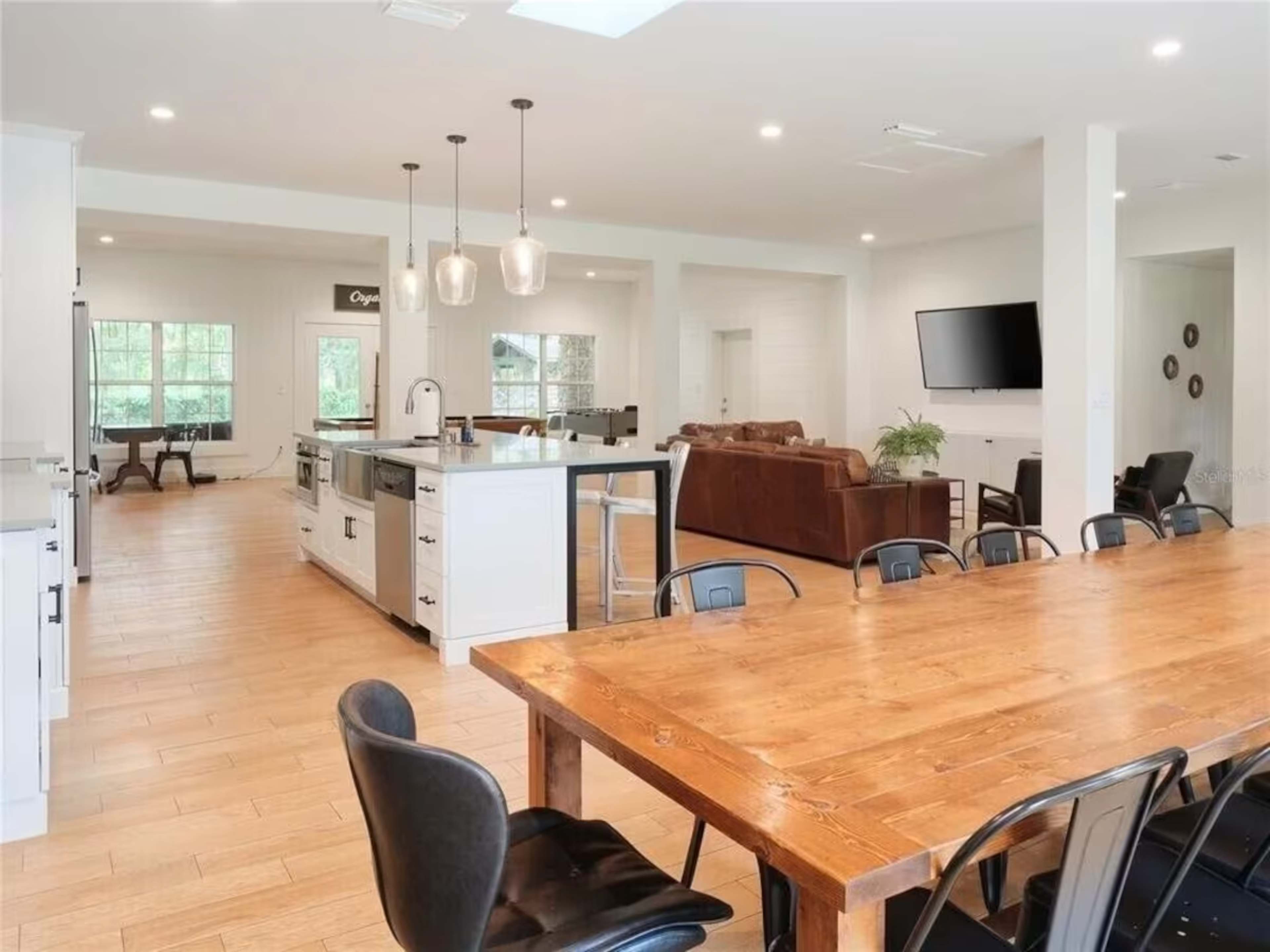 A modern open-concept kitchen and dining area featuring a large wooden table, pendant lighting, and ample natural light.