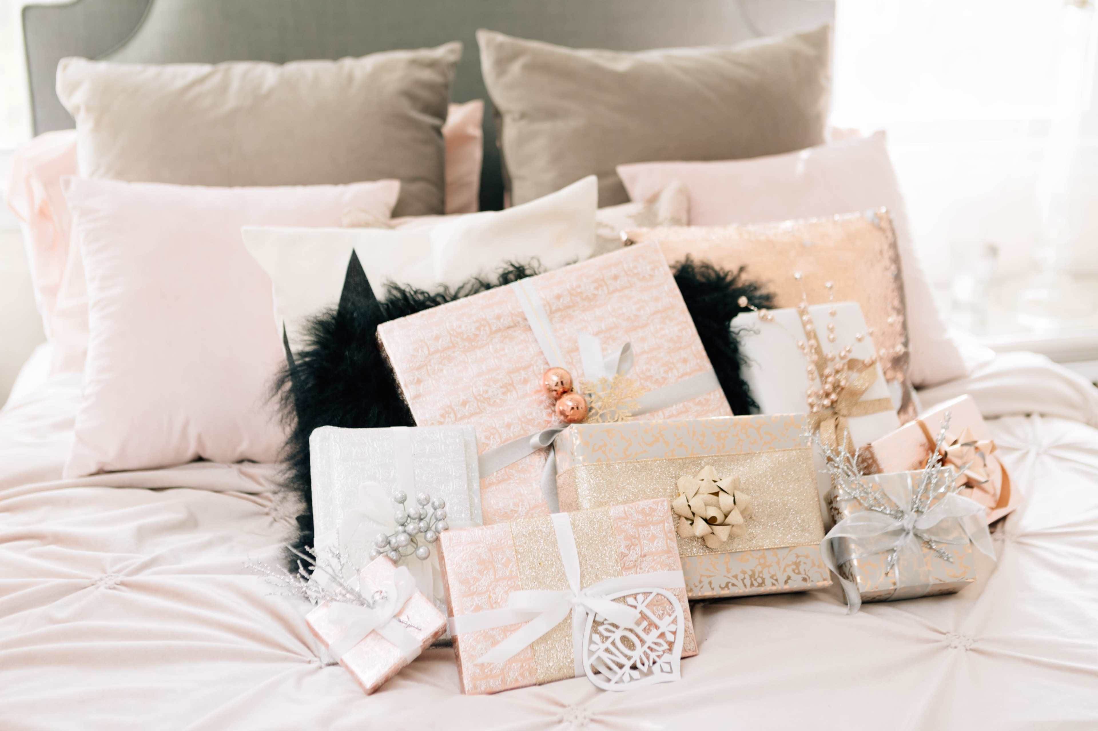 A group of decorated gift boxes in various sizes is arranged on a bed with plush pillows and a soft throw.