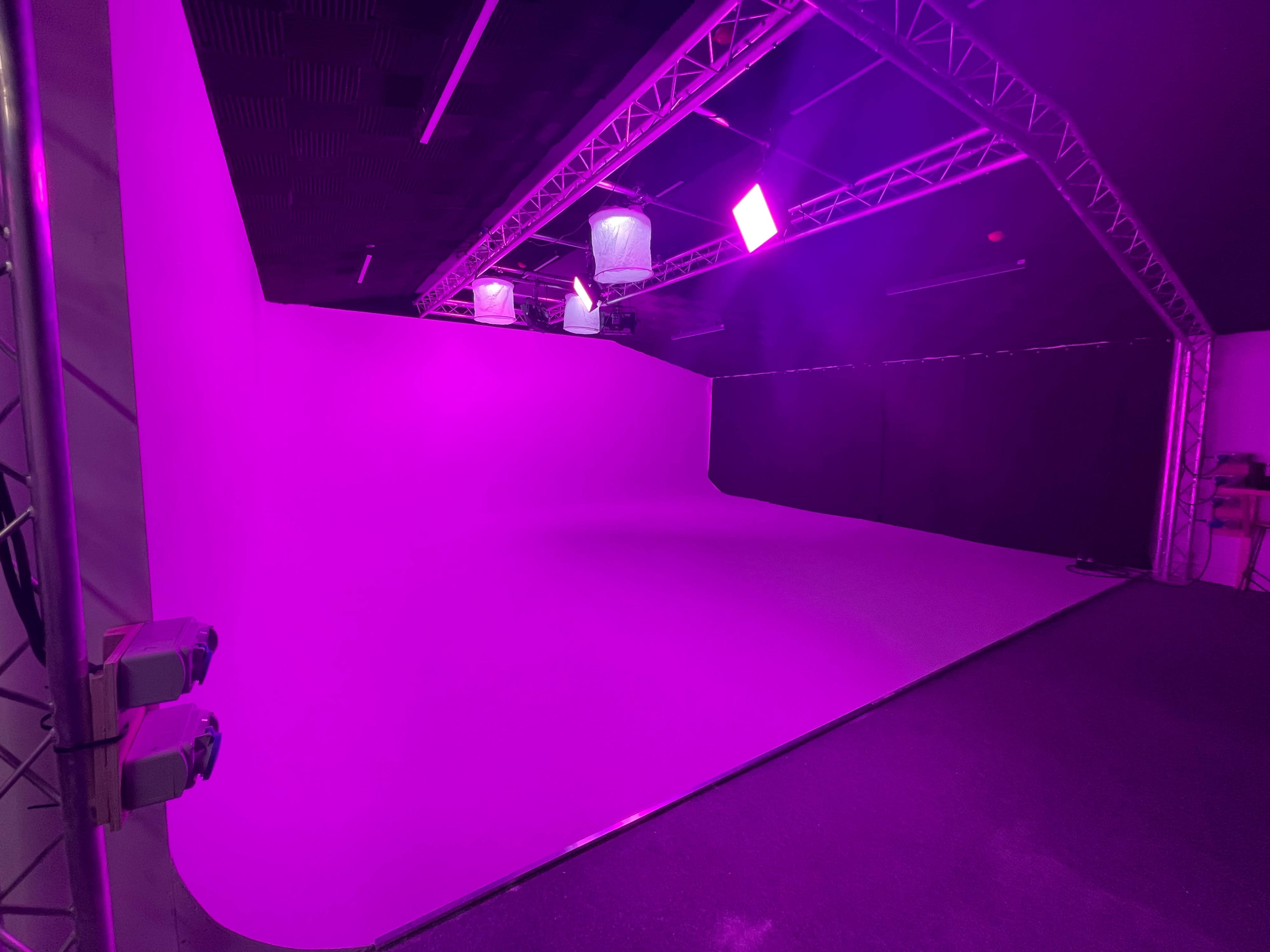A studio space with a seamless purple backdrop and dim lighting from overhead fixtures.