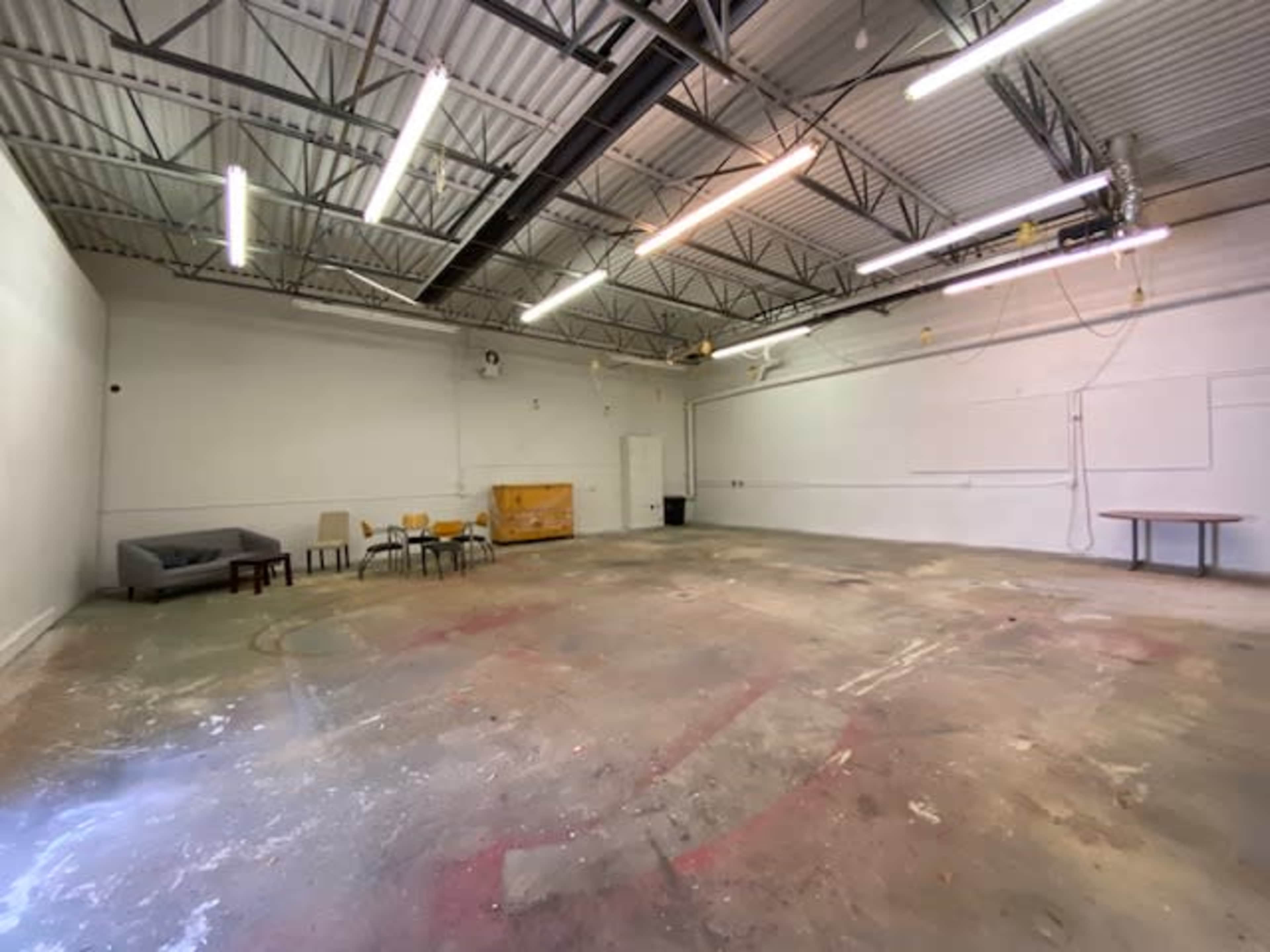 A spacious, unfinished room with a concrete floor, scattered furniture, and overhead lighting.