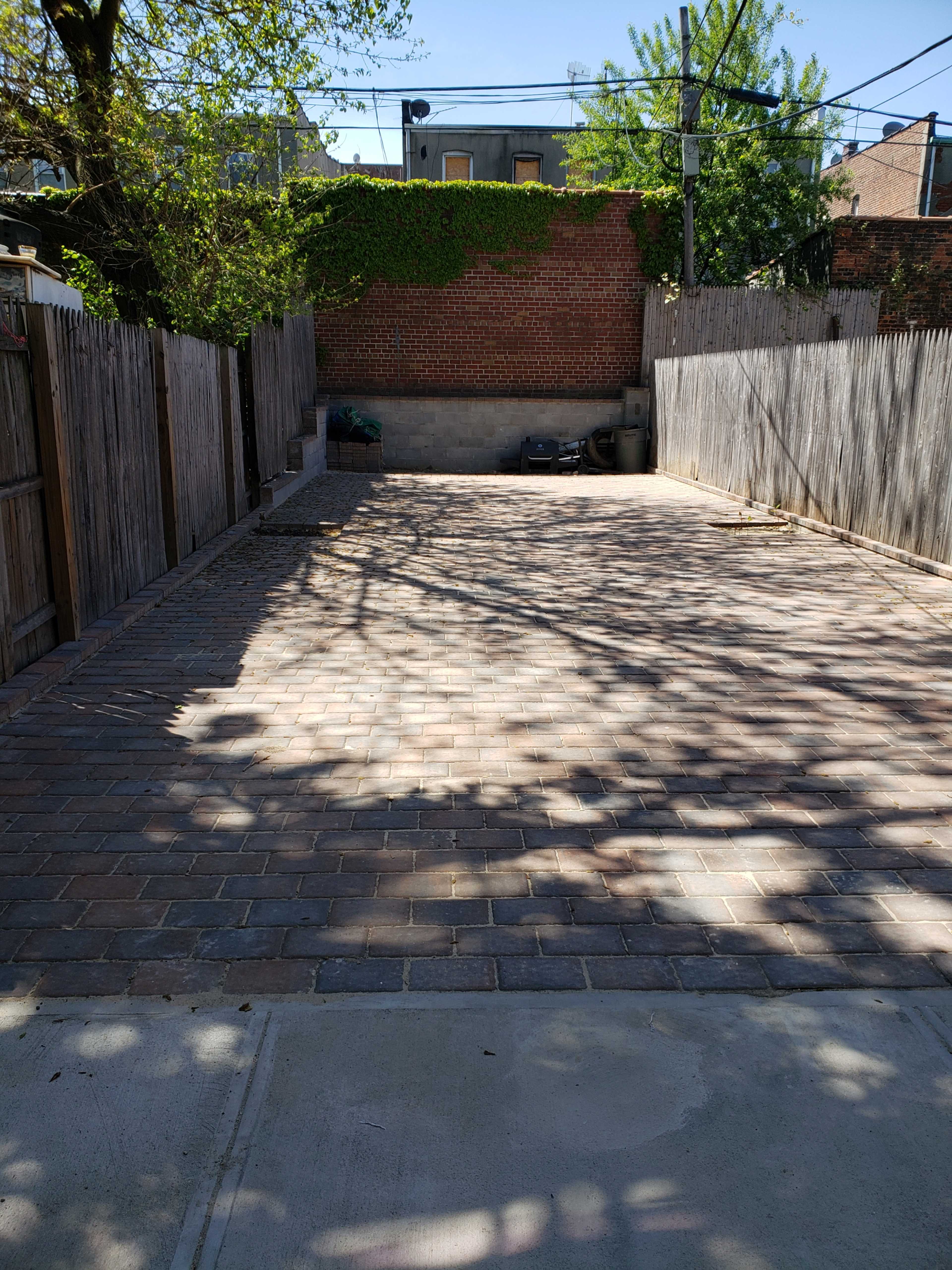 A paved outdoor area surrounded by wooden fences and shaded by trees.