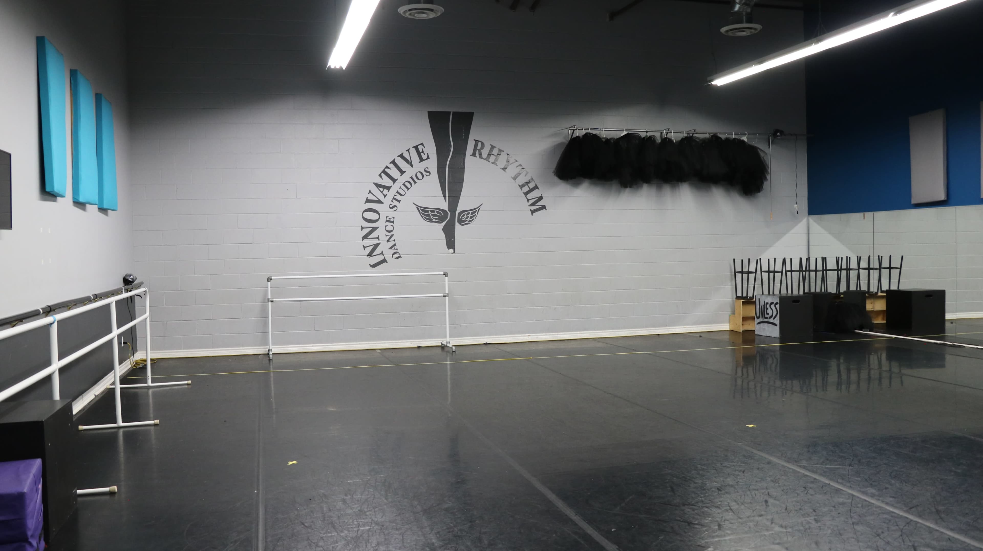 The image shows a dance studio with a polished floor, ballet barres along one wall, and a mural featuring the words "Innovative Rhythm" on another wall.