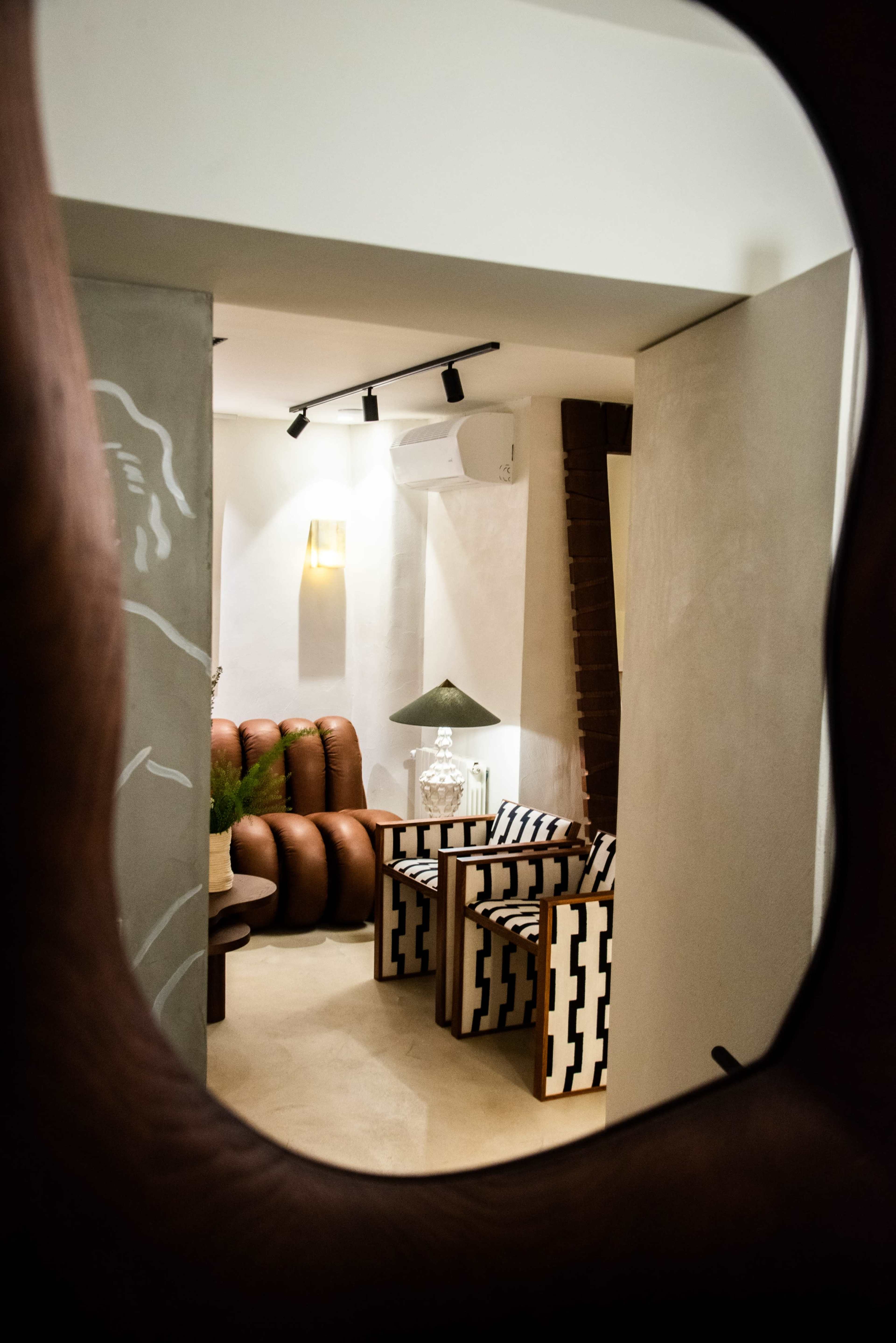 A modern interior features brown leather seating and patterned chairs, visible through an ornate mirror frame.