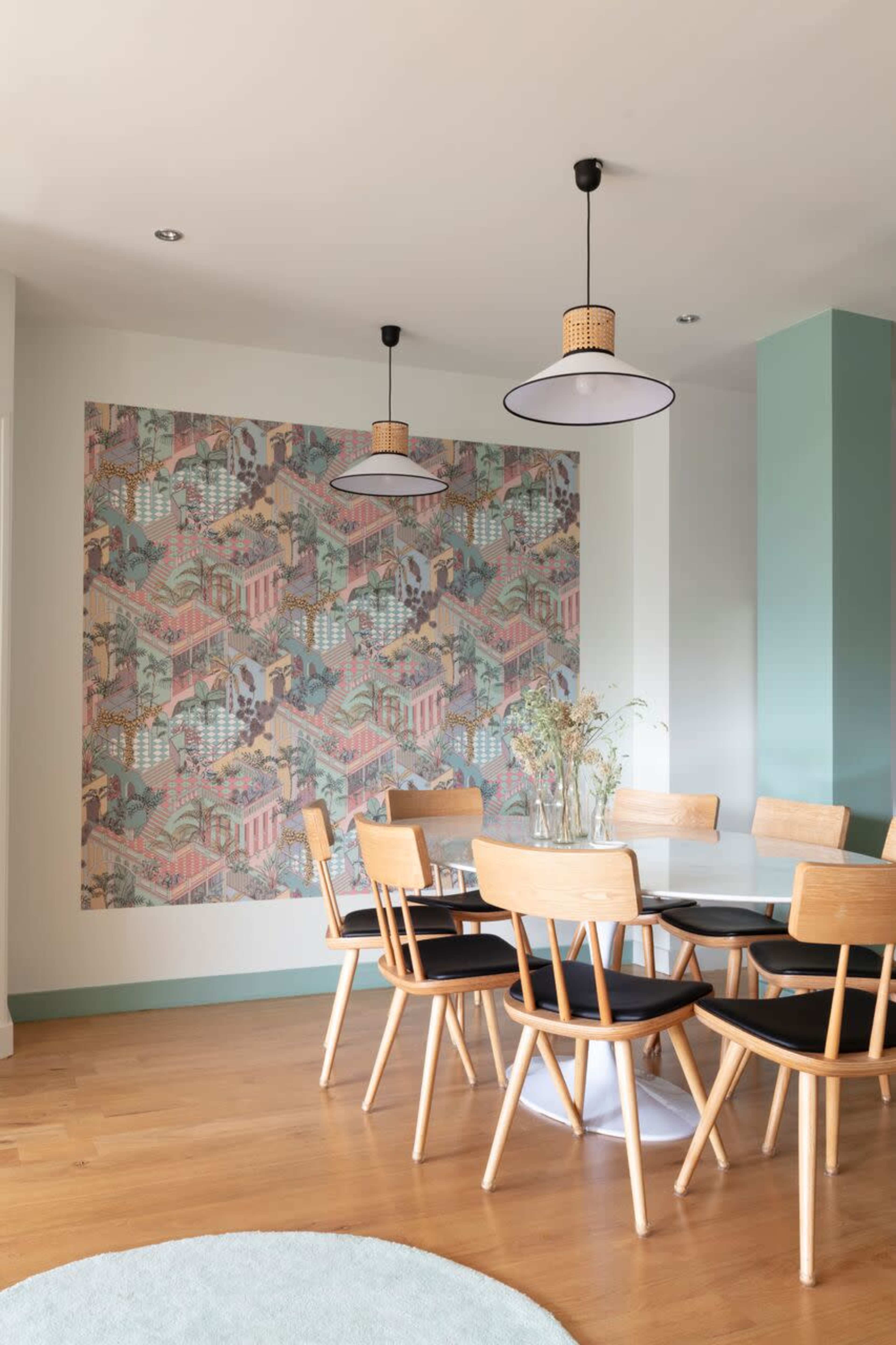 A dining area features a round table surrounded by wooden chairs, with a patterned mural on one wall and pendant lighting above.