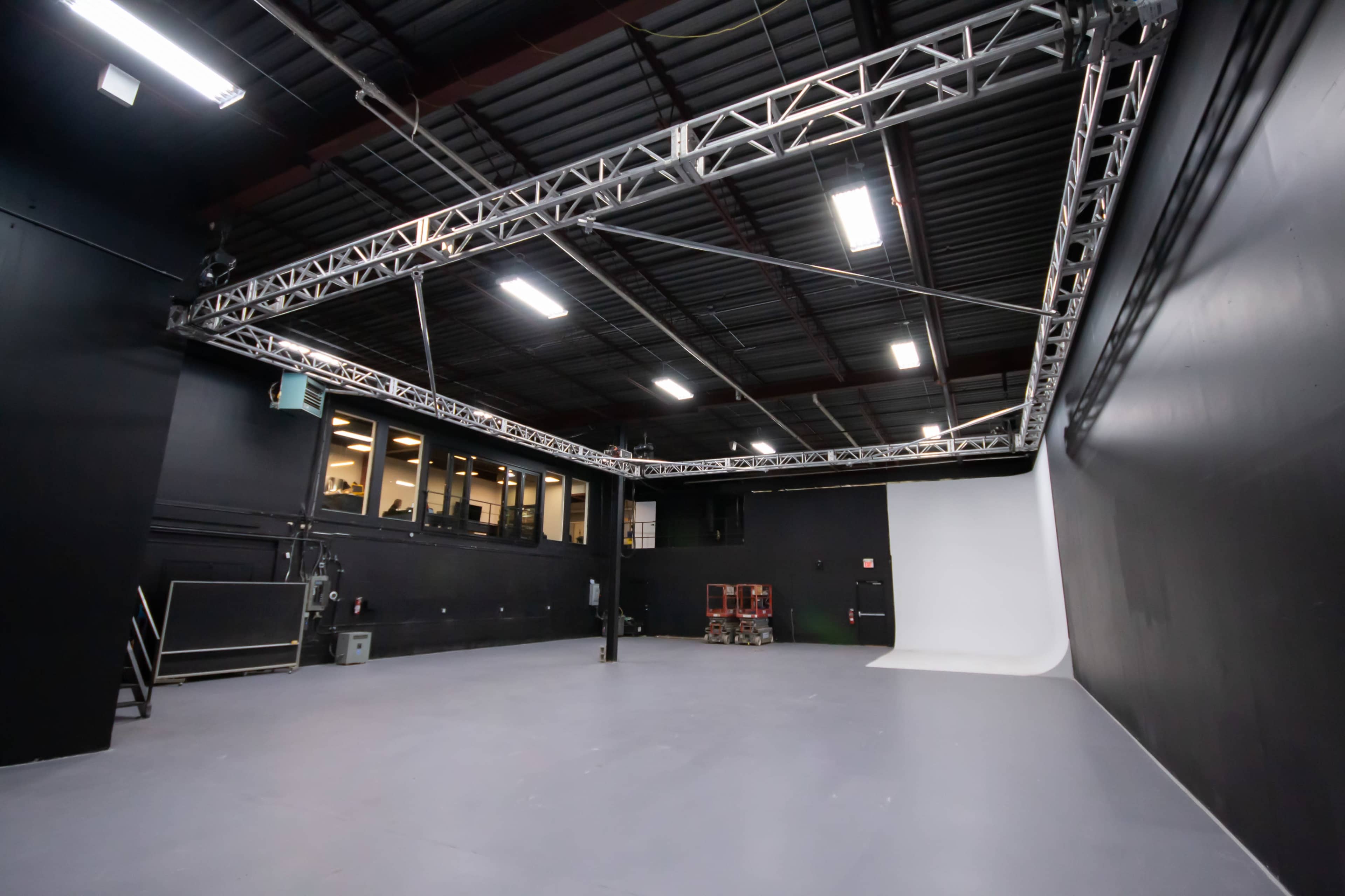 An empty photography studio with black walls, a gray floor, and a white backdrop at one end.