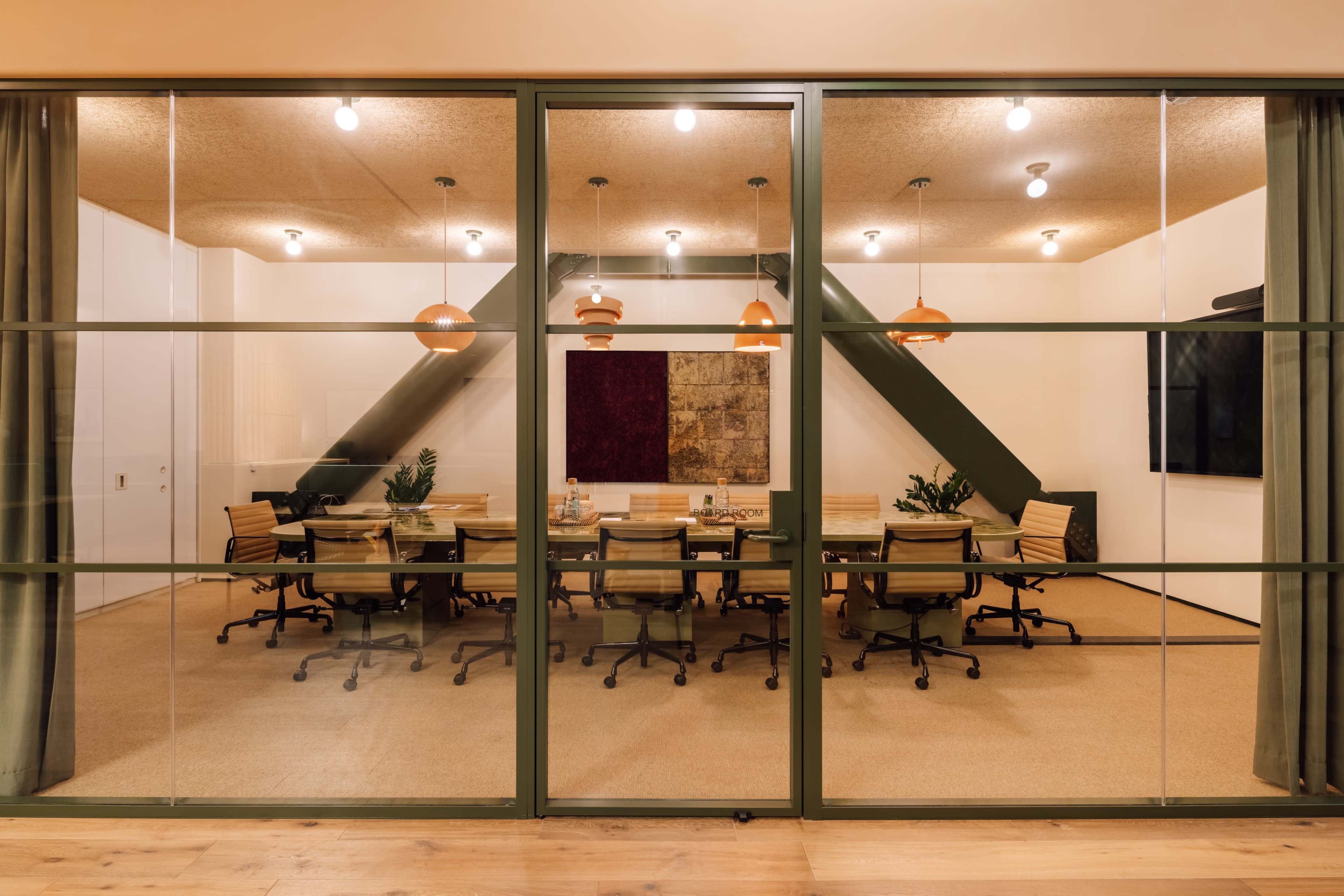 A conference room with a large table surrounded by chairs is visible through glass walls, featuring overhead lighting and decorative artwork.