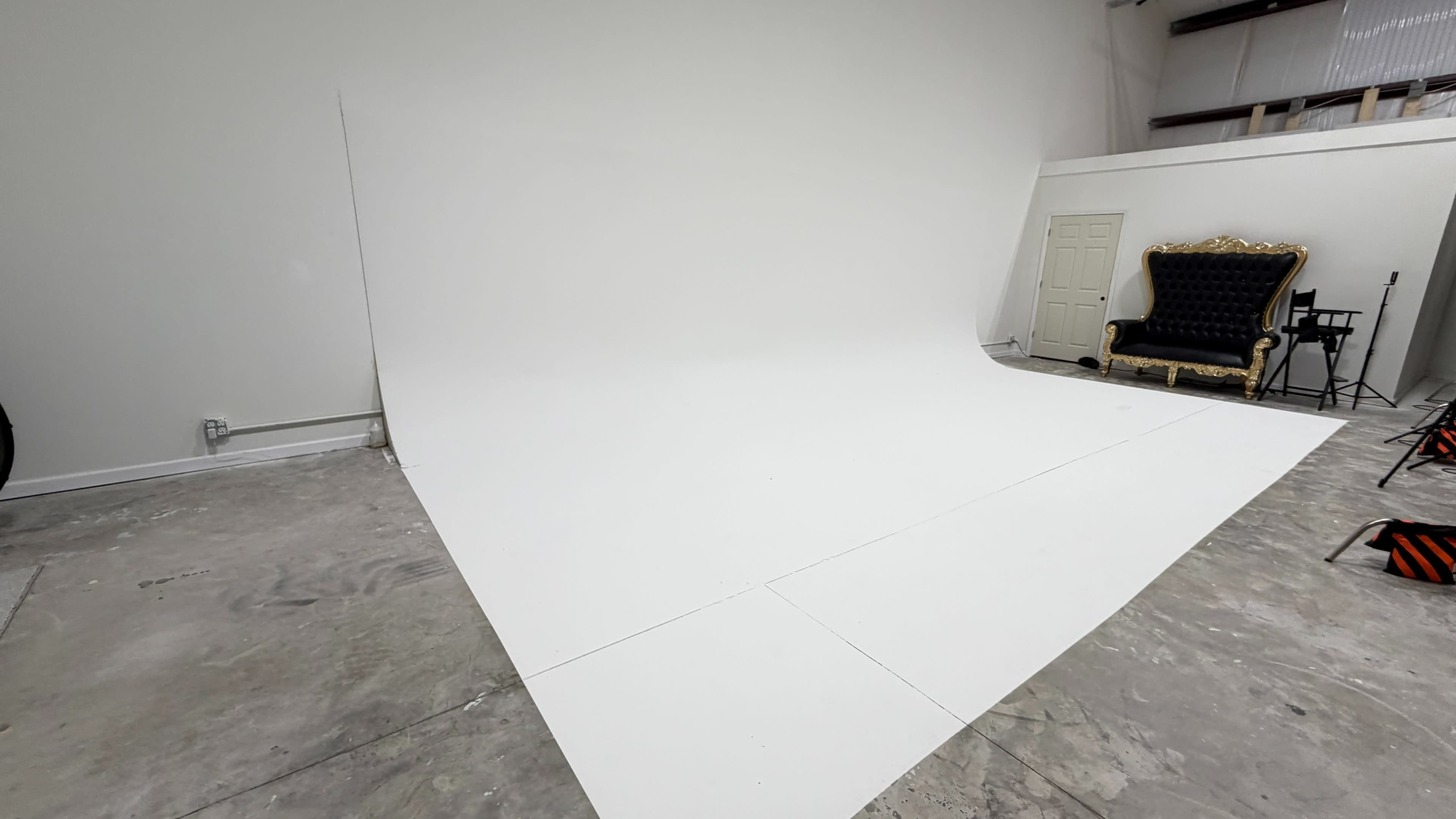 The image shows an empty photography studio with a white backdrop, a gold-framed chair, and a light gray floor.