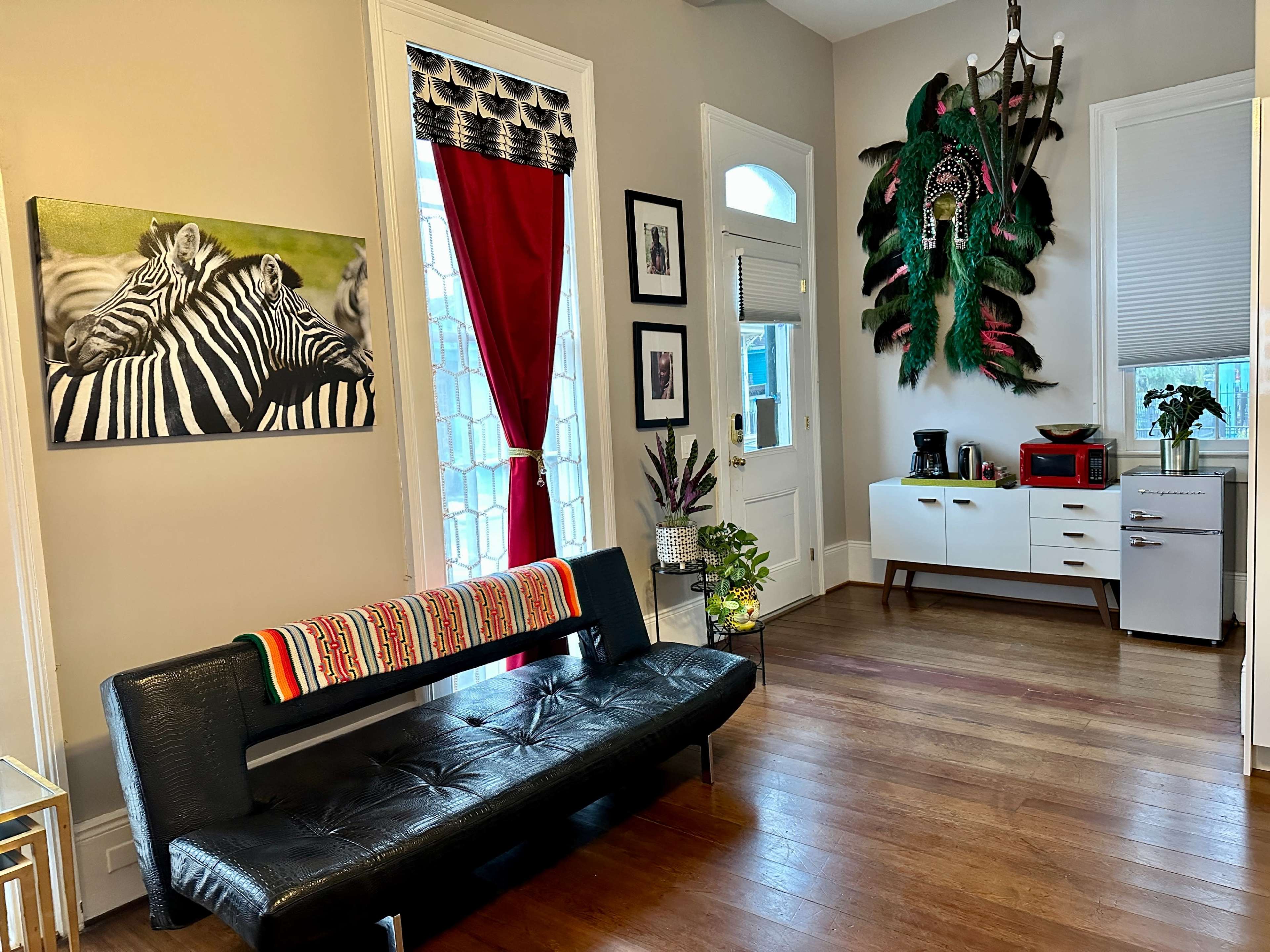 The image shows a cozy living area featuring a black bench, a zebra-striped artwork on the wall, a red curtain, and a white furniture set with a small refrigerator and coffee maker.