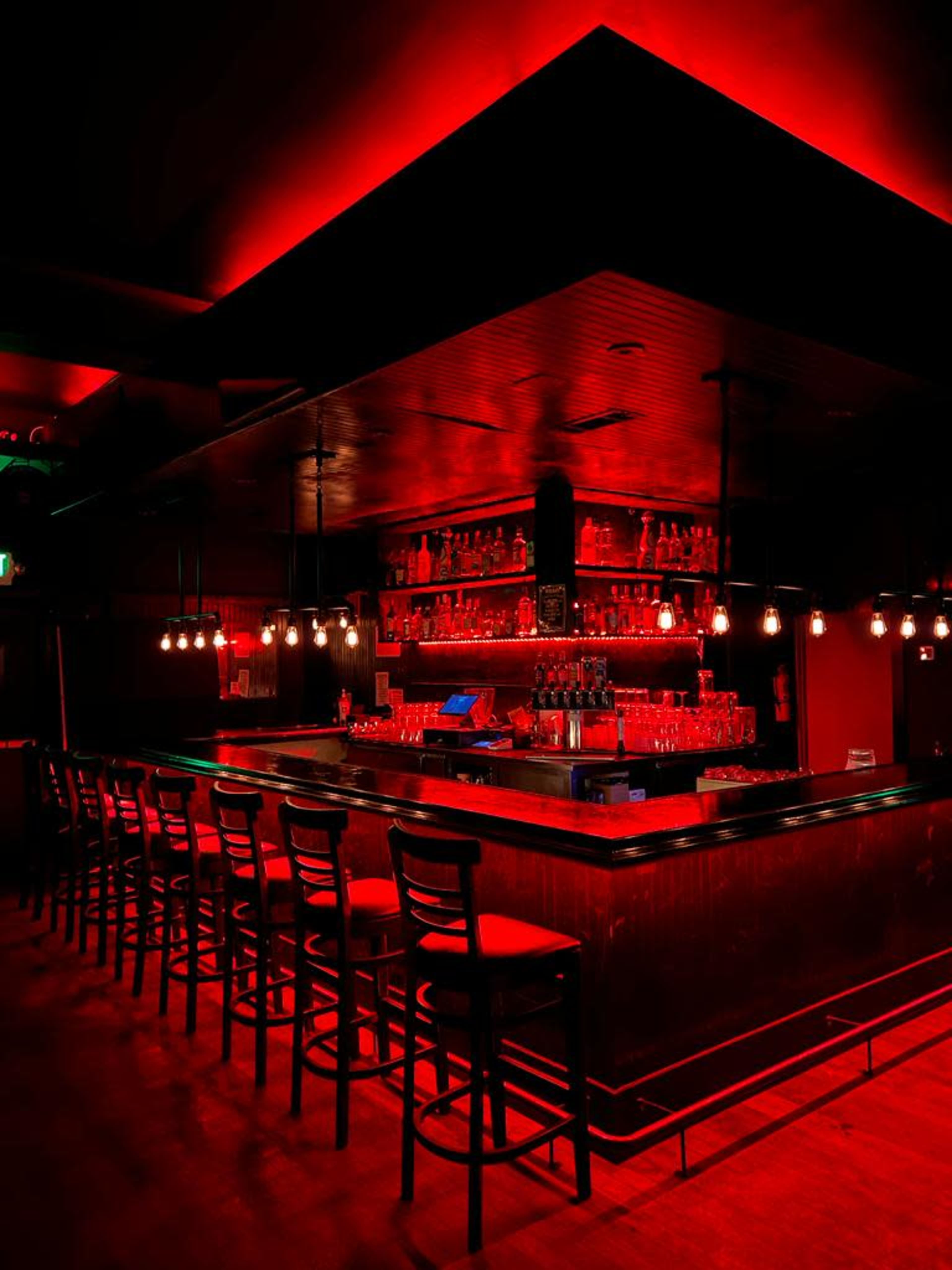 A dimly lit bar with red lighting and a long counter lined with empty chairs.