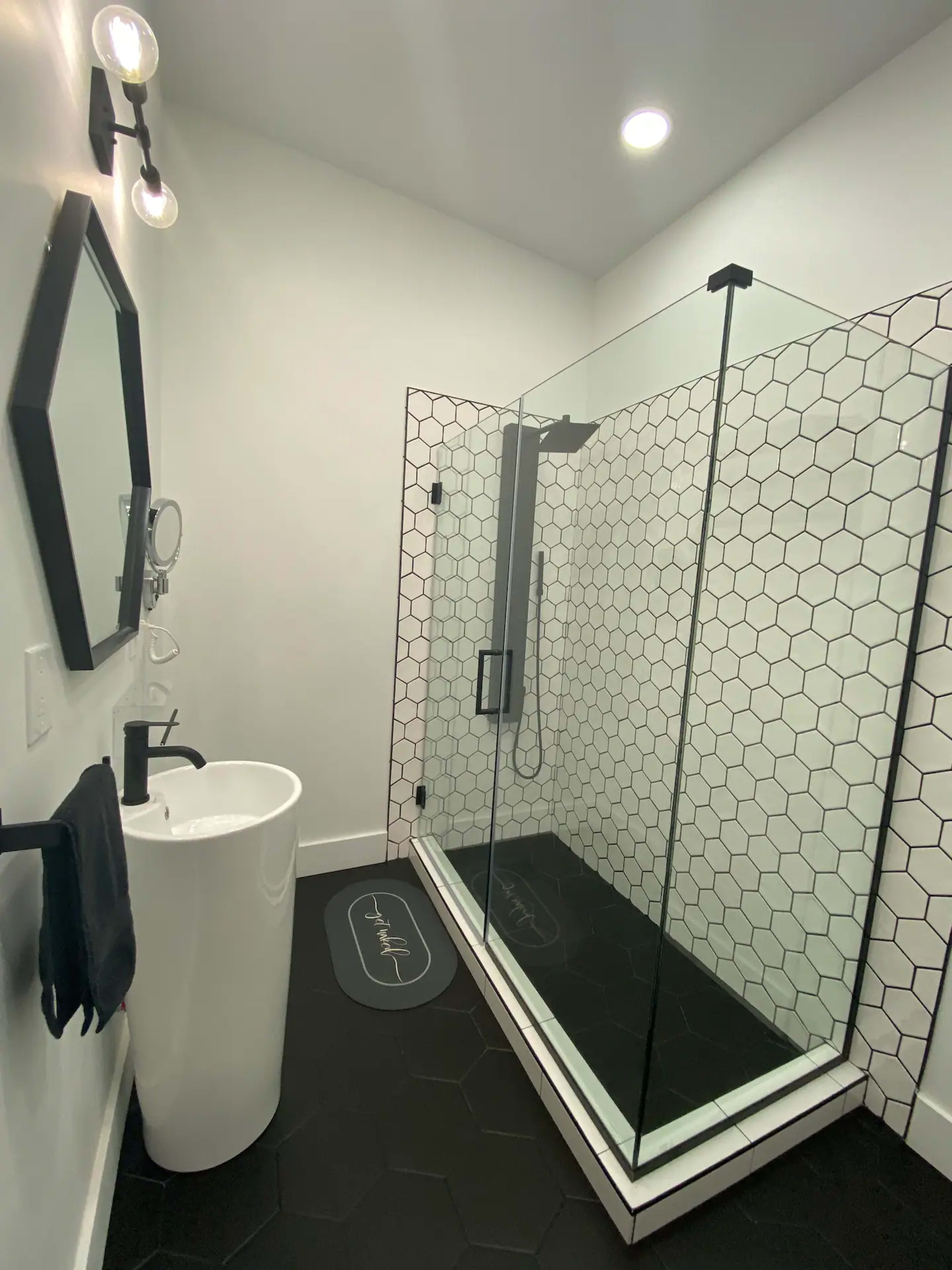 A modern bathroom featuring a glass shower enclosure with hexagonal tile walls, a freestanding sink, and a dark floor.