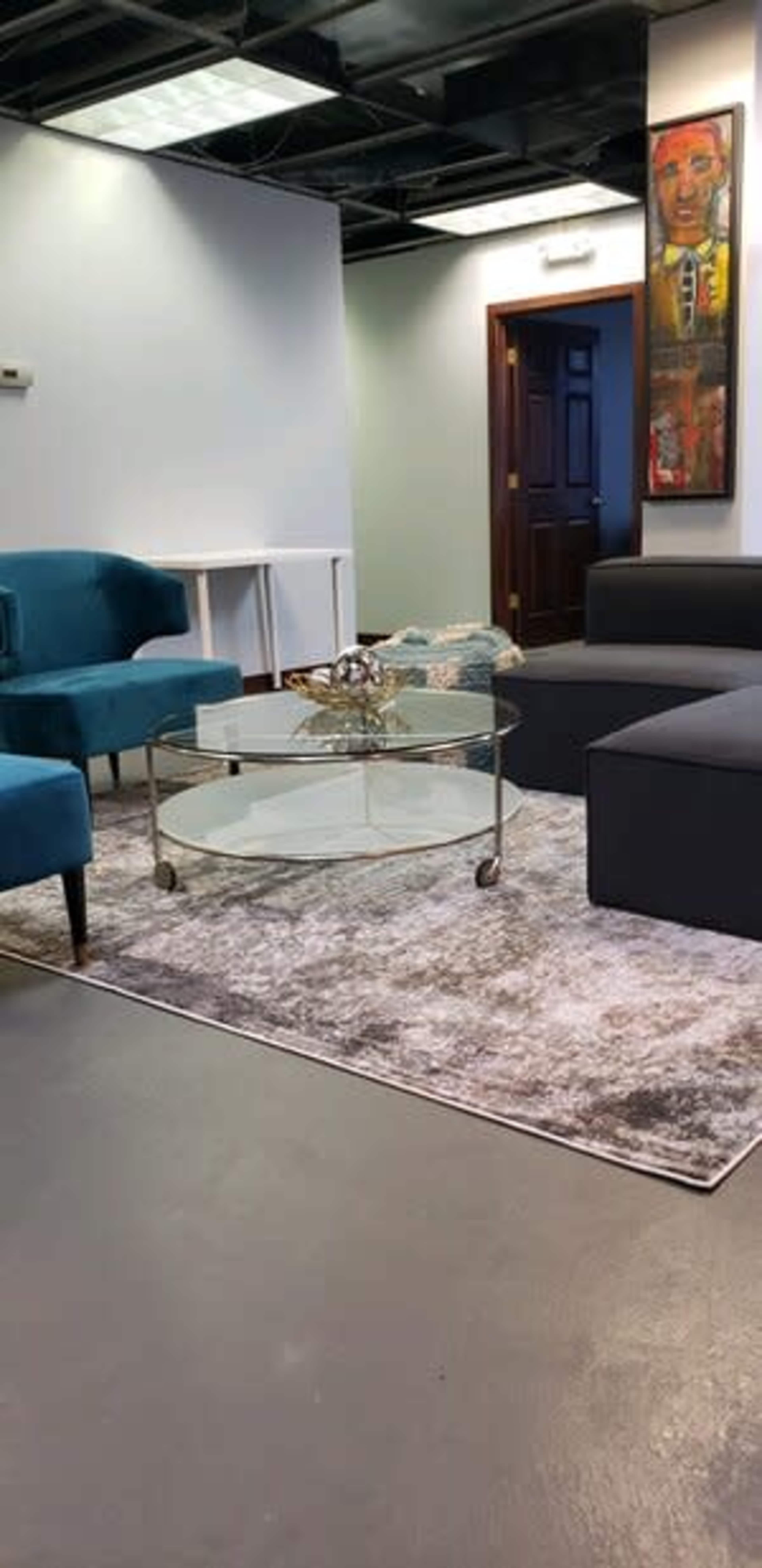 The image shows a modern office interior featuring two sofas, a glass coffee table, and a decorative rug.