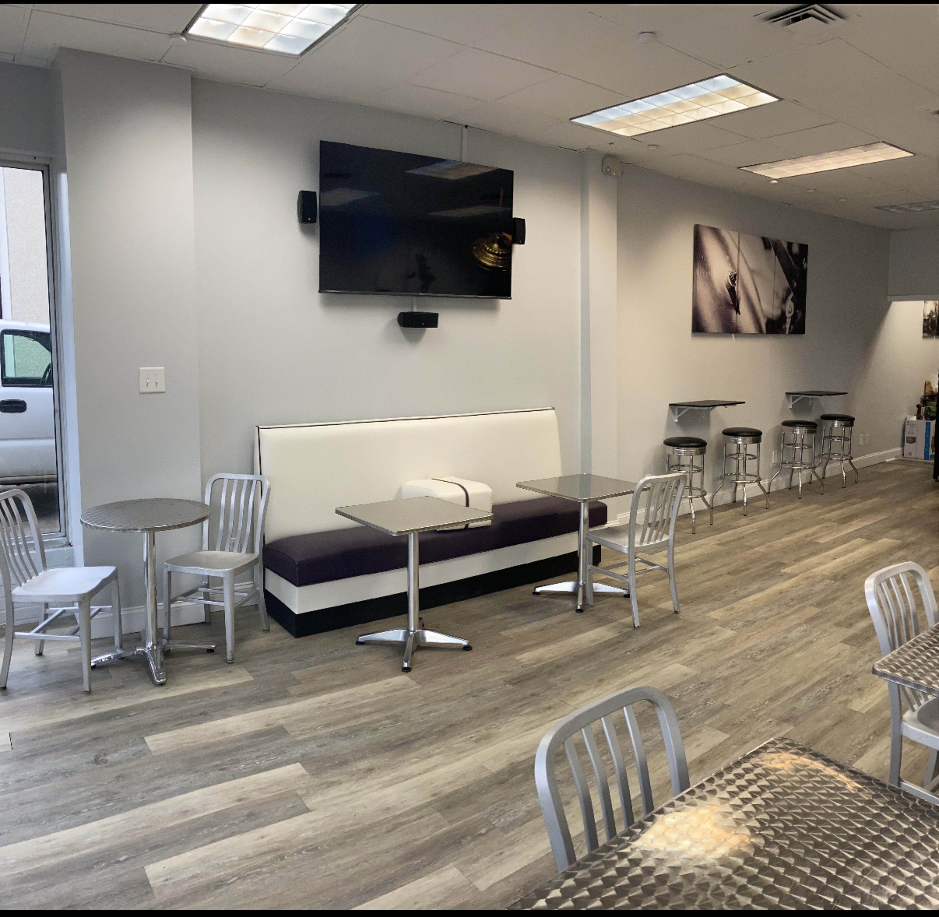 The image shows a modern, empty cafe interior with tables and chairs, a wall-mounted television, and large windows letting in natural light.