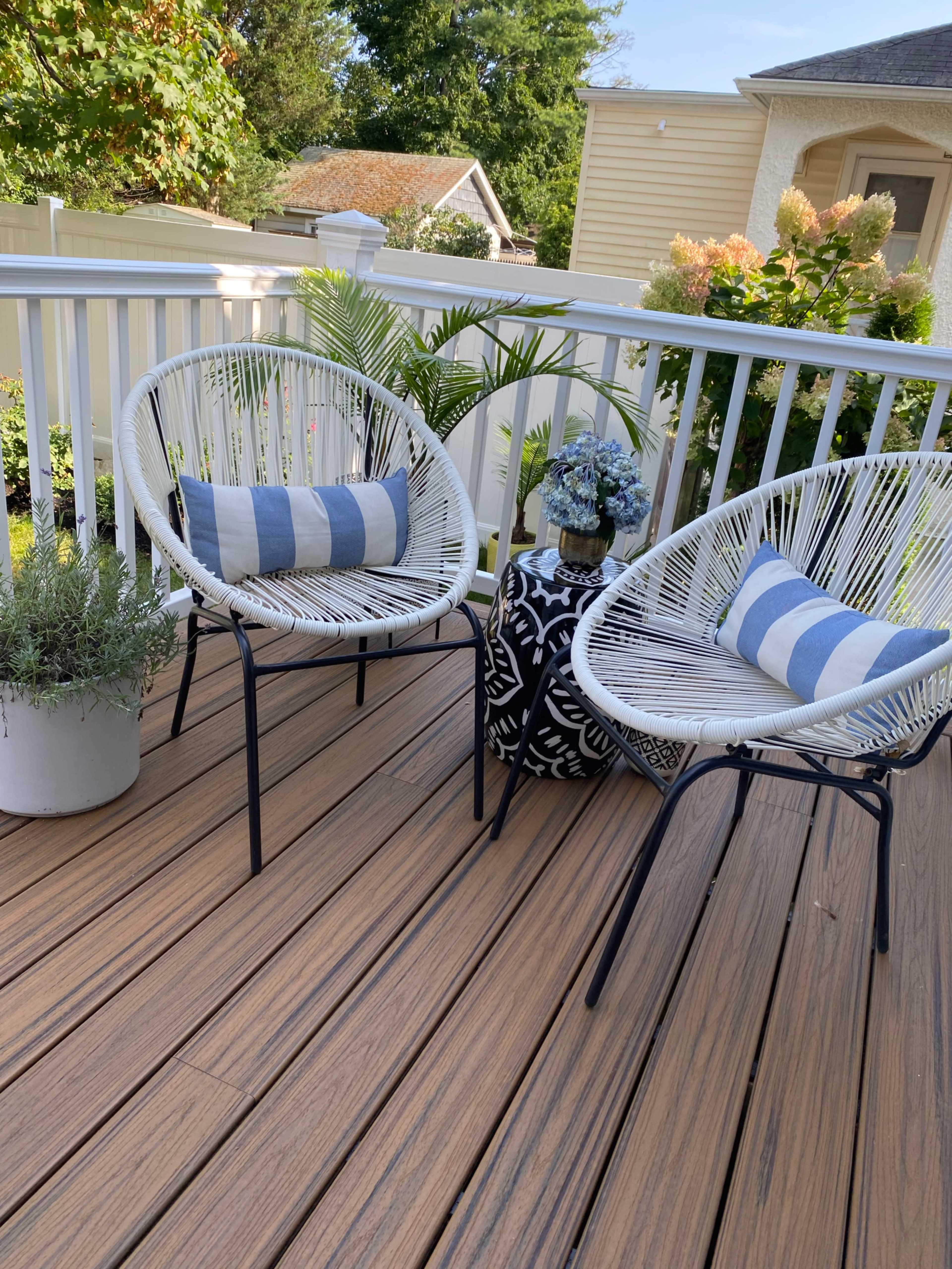 A patio with two white acapulco chairs, a small black and white circular table, and a potted plant on a wooden deck.