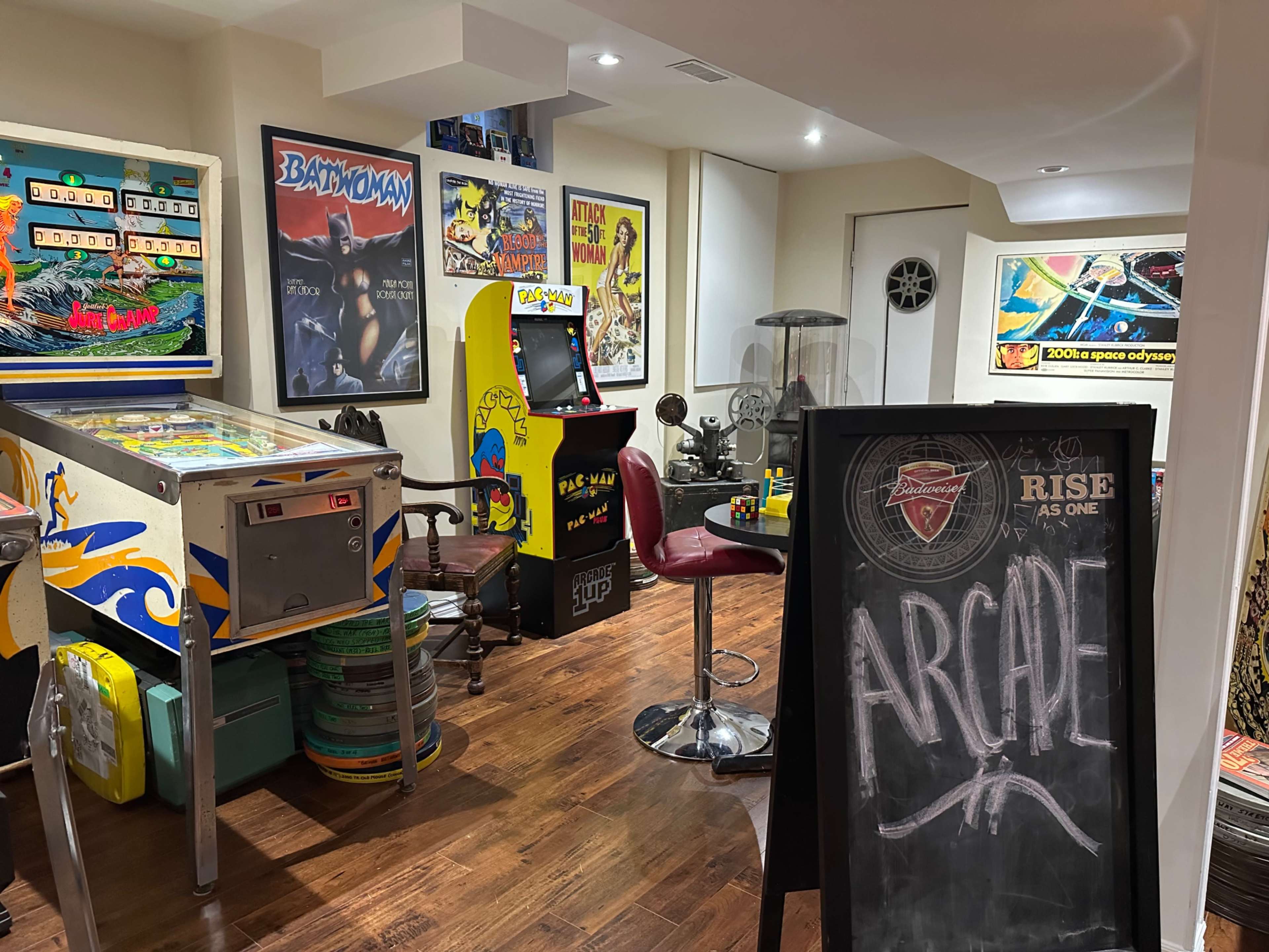 The image shows a basement arcade featuring vintage pinball machines, arcade games, and retro posters on the walls.