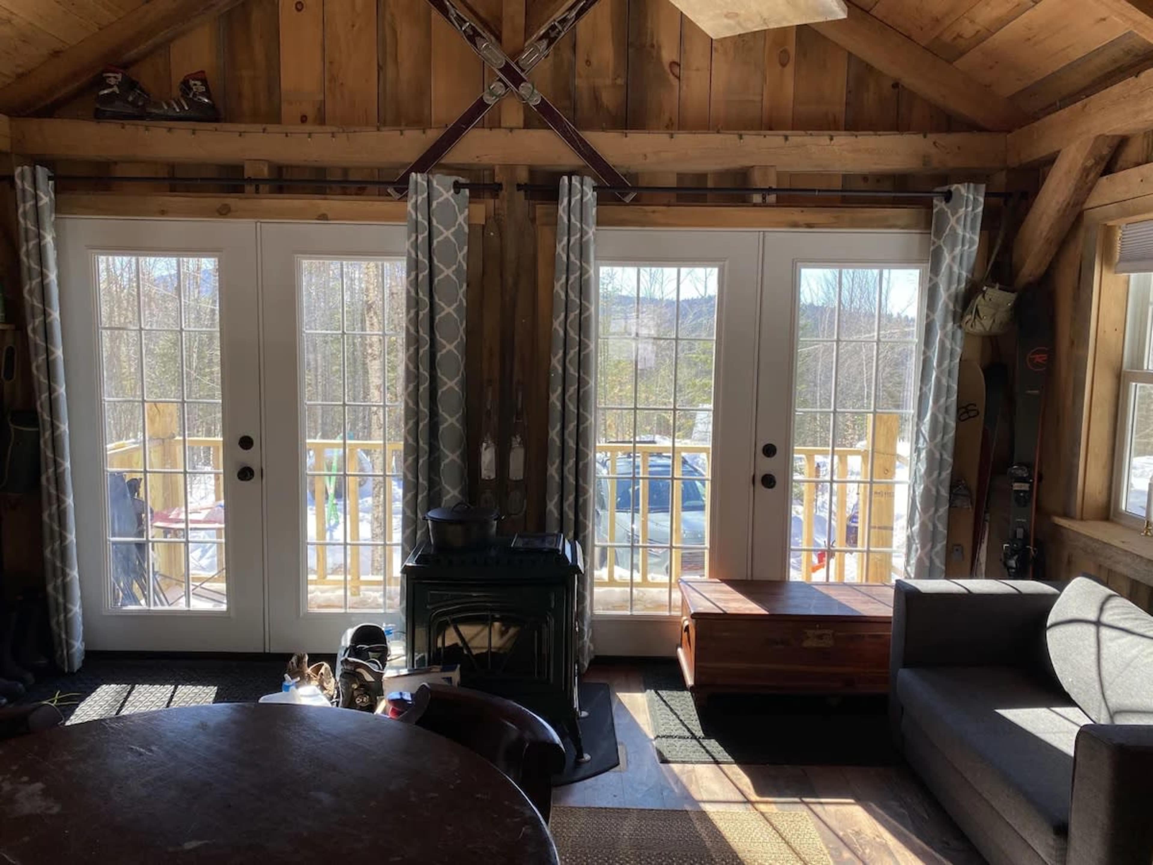 A cozy cabin interior featuring two sets of double doors leading to a deck, with a circular dining table and a couch nearby.